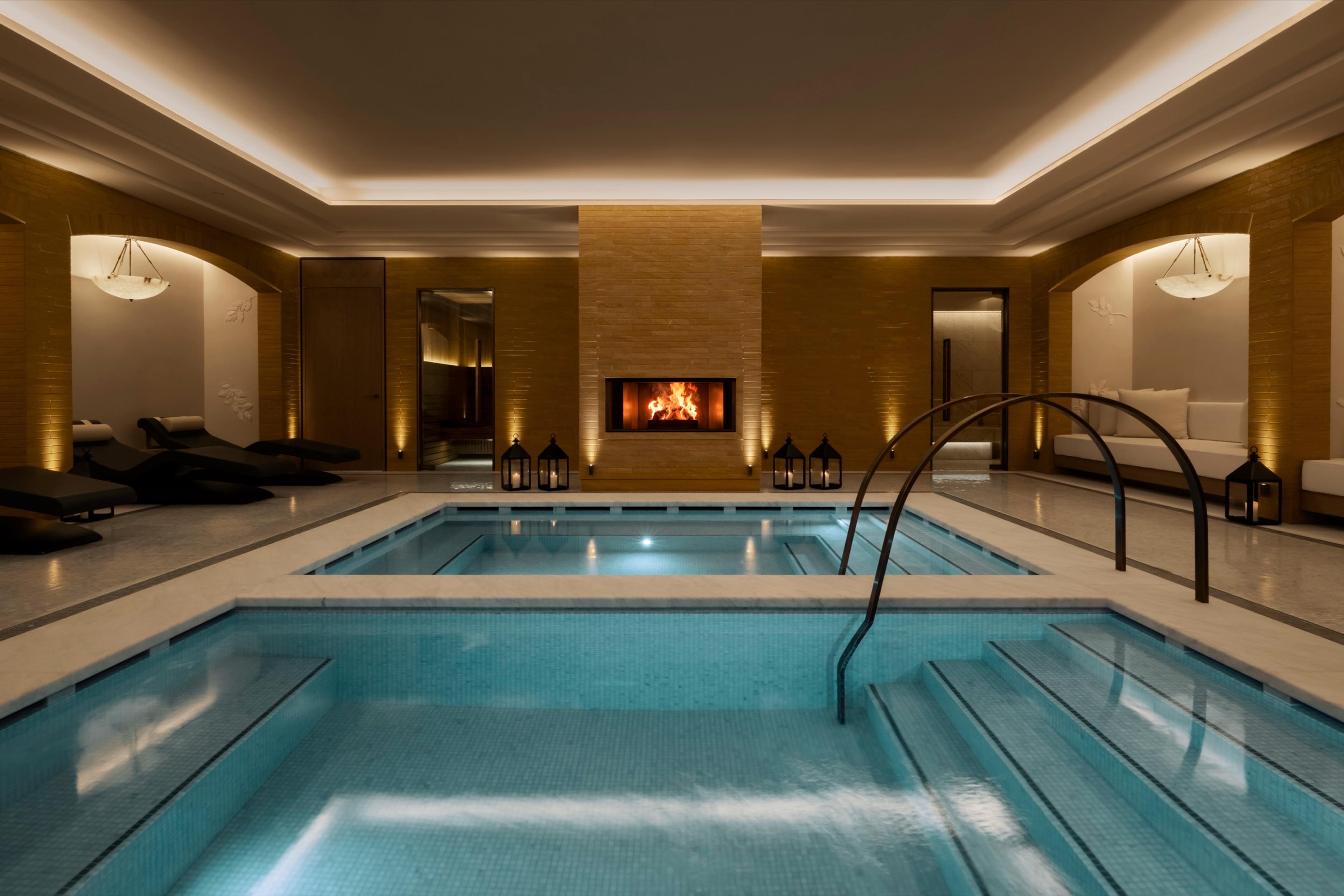 a hydrotherapy pool lit by lanterns, steps leading down into the water, with a lit fireplace and loungers behind