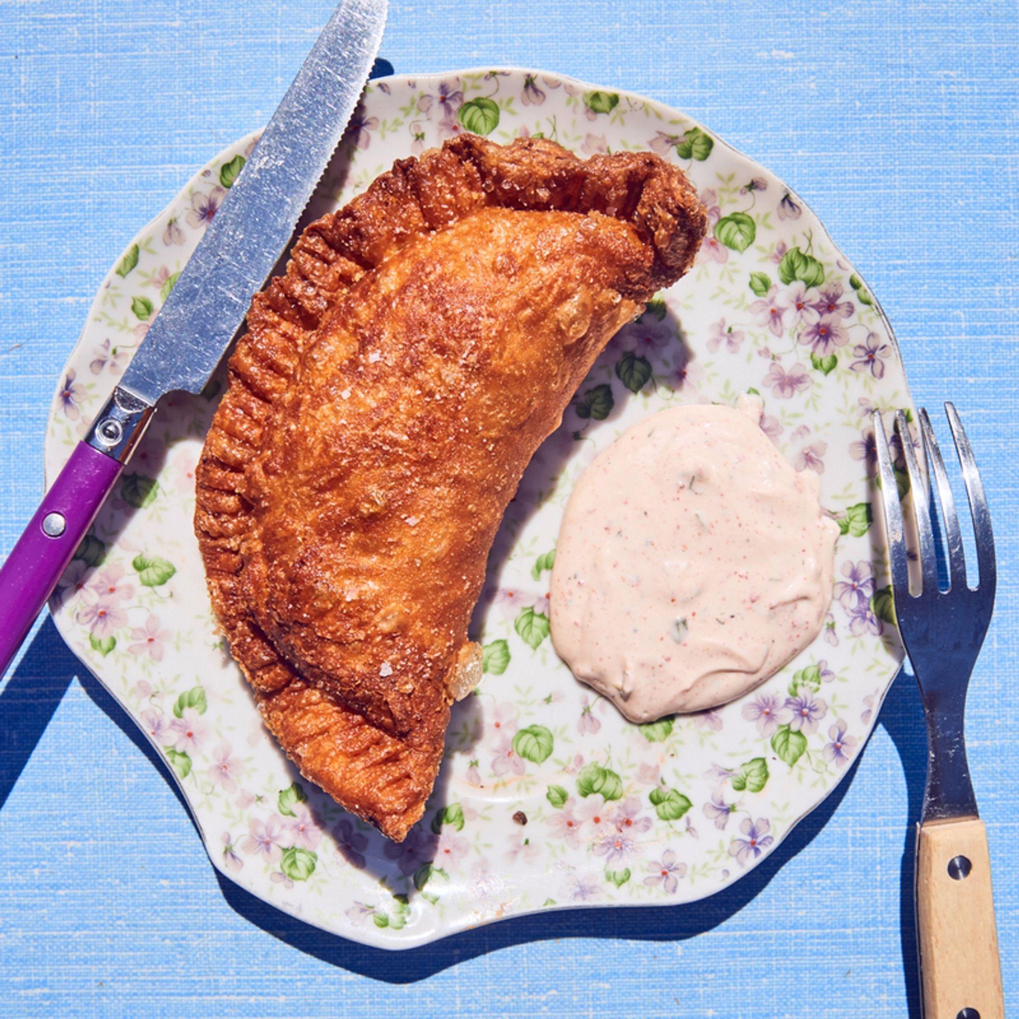A golden fried hand pie with a pink dipping sauce, on a floral plate