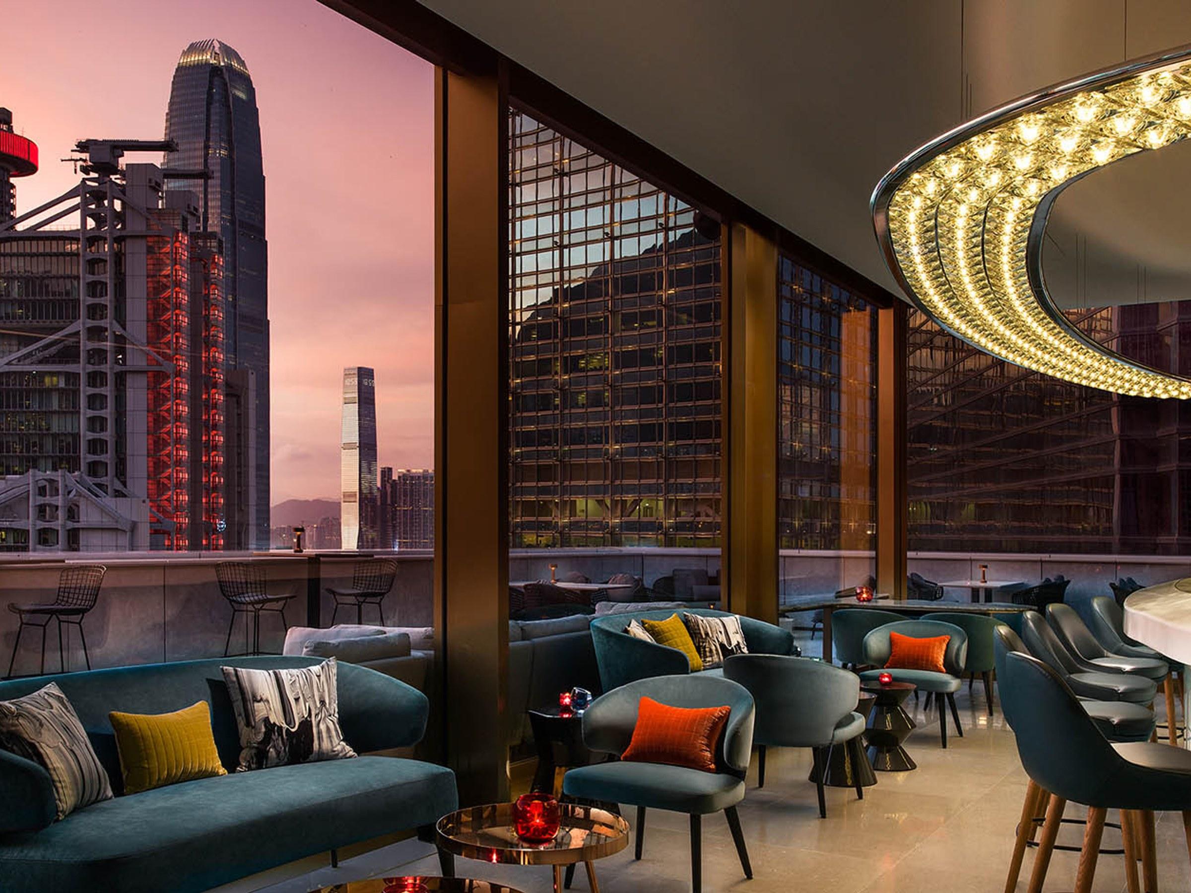 A rooftop bar of teal sofas looking out on Central's towers at dusk