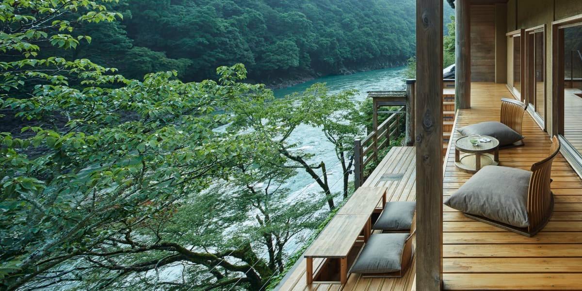 A wooden terrace with floor cushions, looking out through green trees to the river