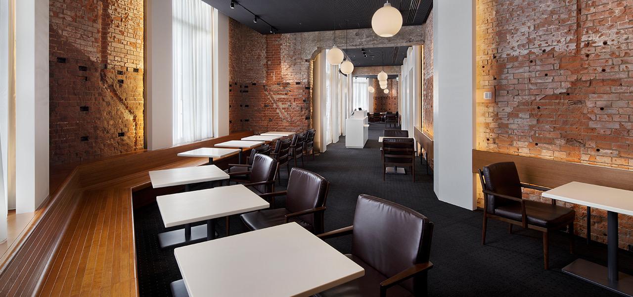 A wider view of a brick-walled restaurant, with rows of white tables and leather chairs leading toward a host stand in the distance.