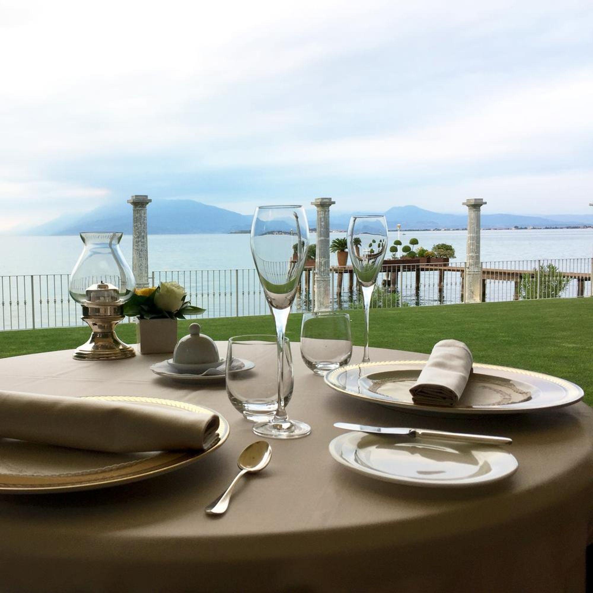 A table laid on a lawn above the lake, a balustrade and the far shore beyond