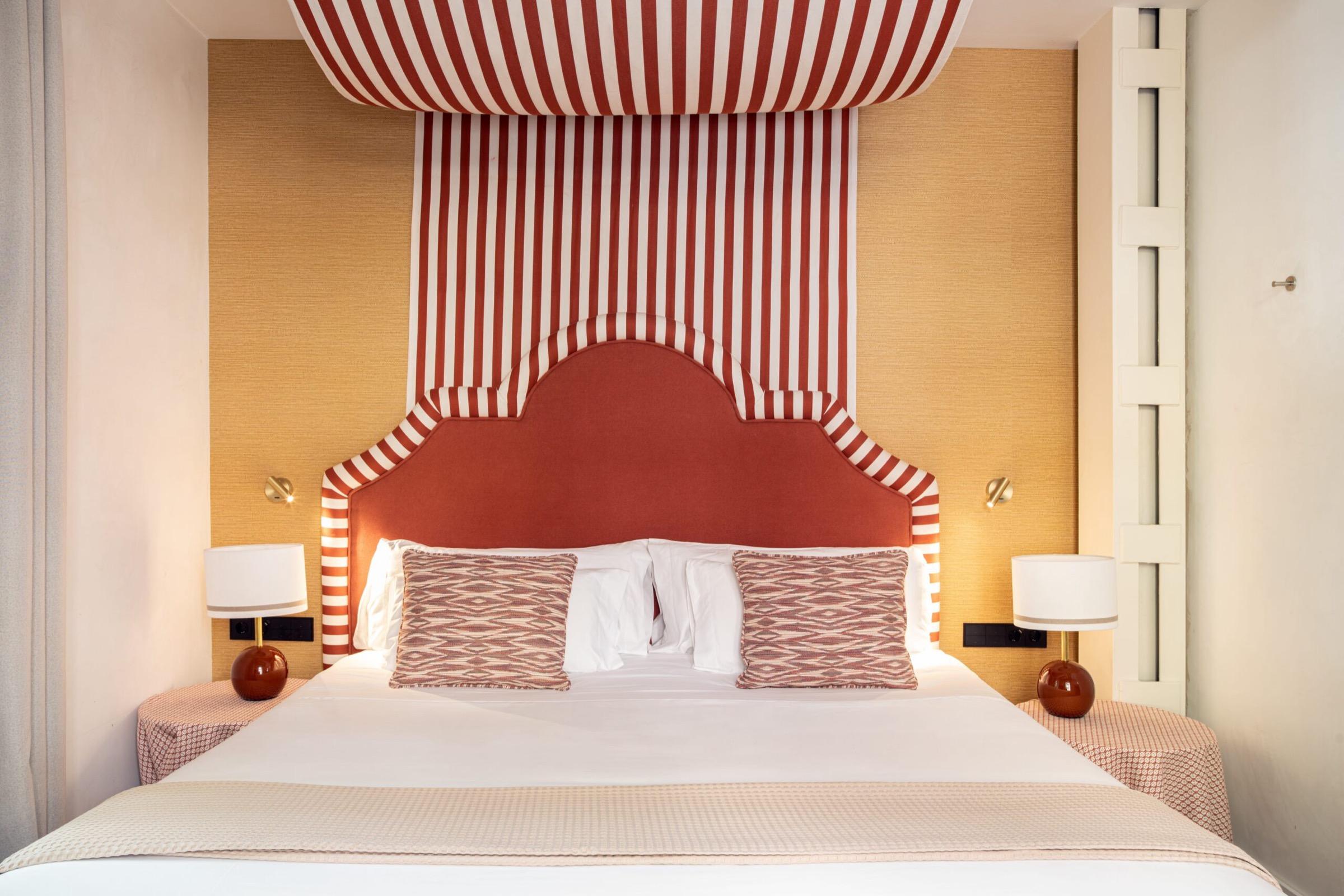 a bed with a red and white striped canopy headboard and patterned cushions against a mustard yellow wall