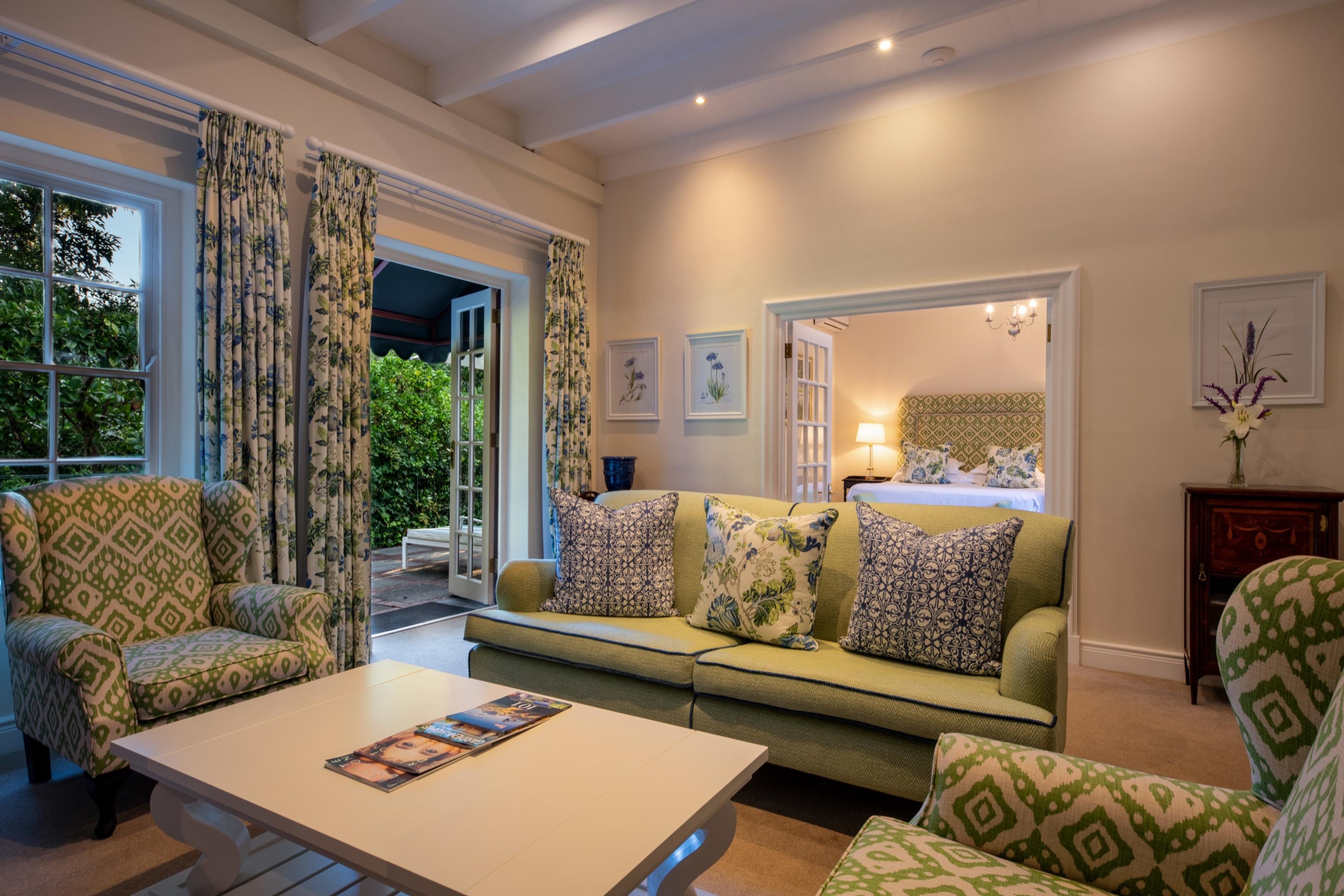A sitting room with a green sofa and armchairs, looking through an open doorway to a bed with a green-patterned headboard.