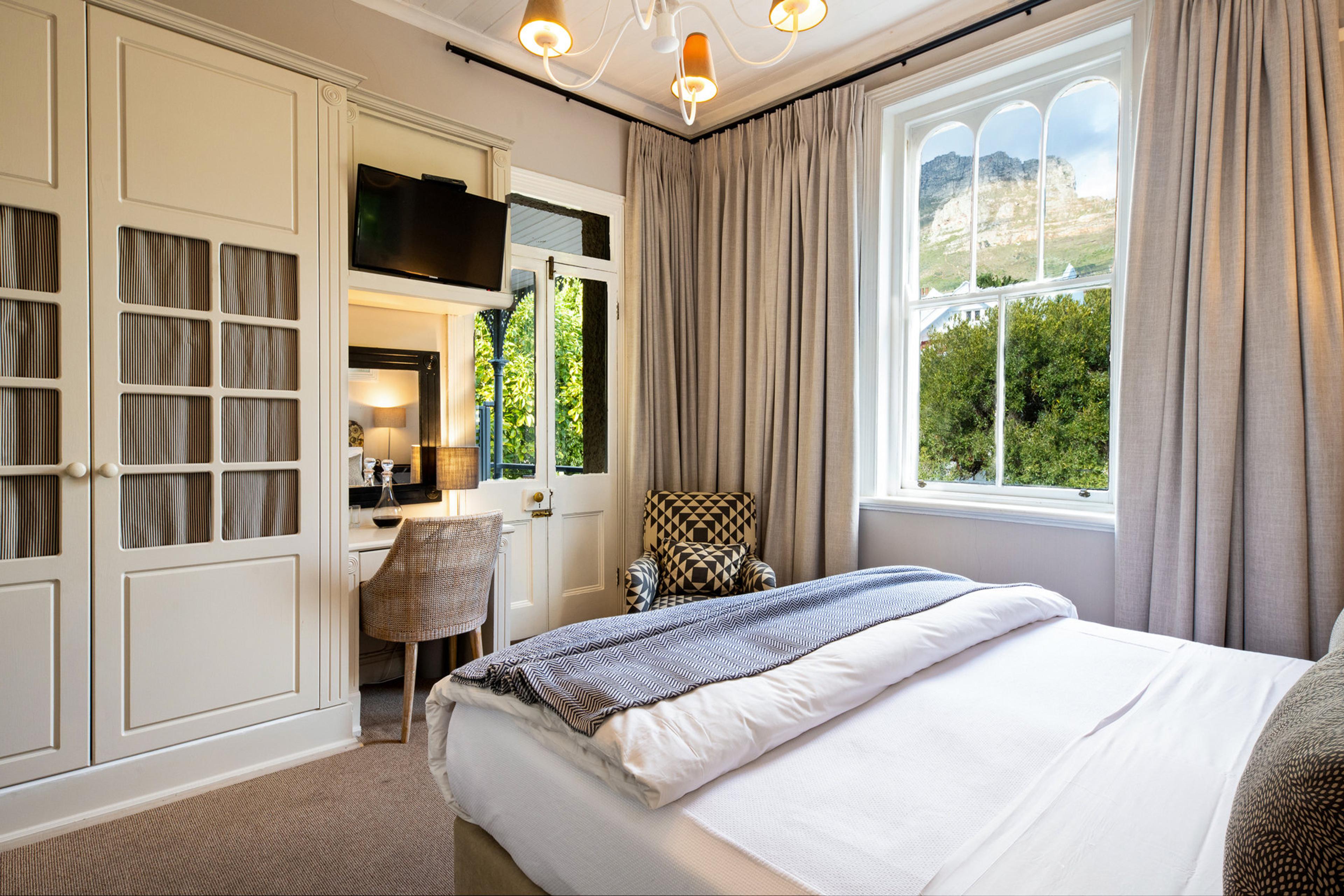 a bedroom with white panelled wardrobes and a sash window framing a mountain with trees below