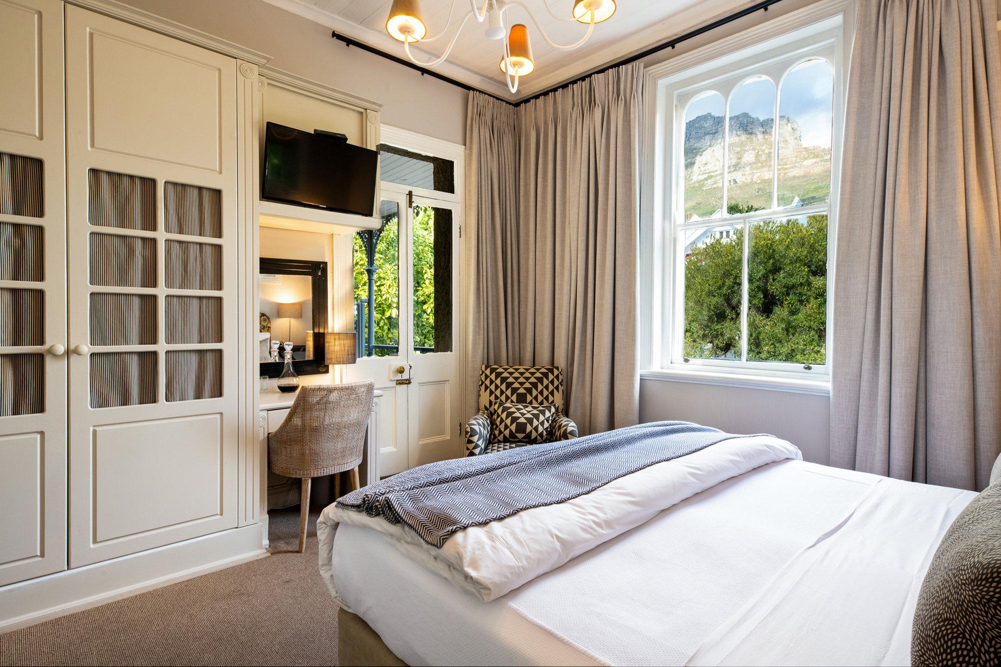 a bedroom with white panelled wardrobes and a sash window framing a mountain with trees below
