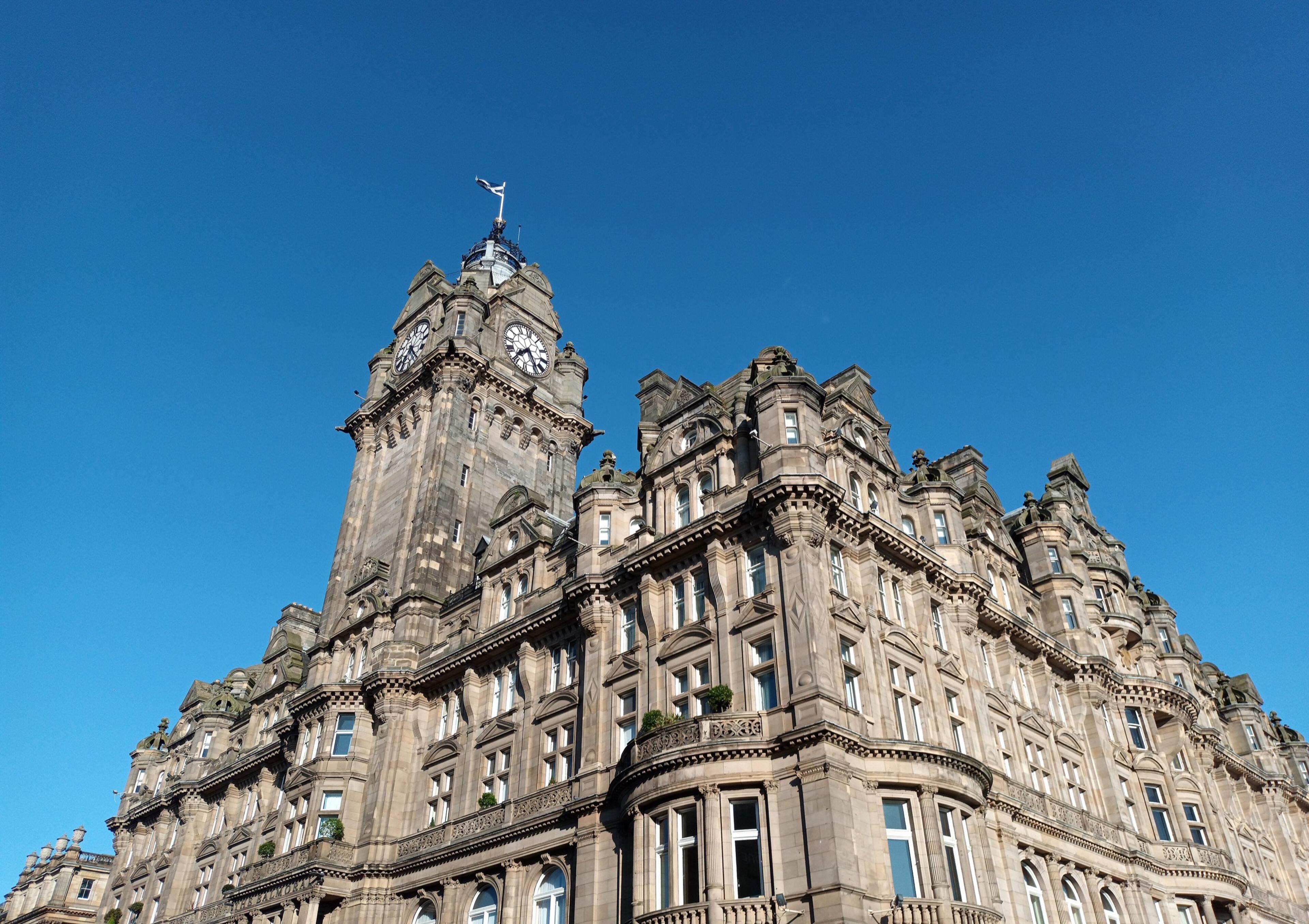 The clock tower of The Balmoral seen from below, rising above its carved sandstone corner against a deep blue sky.