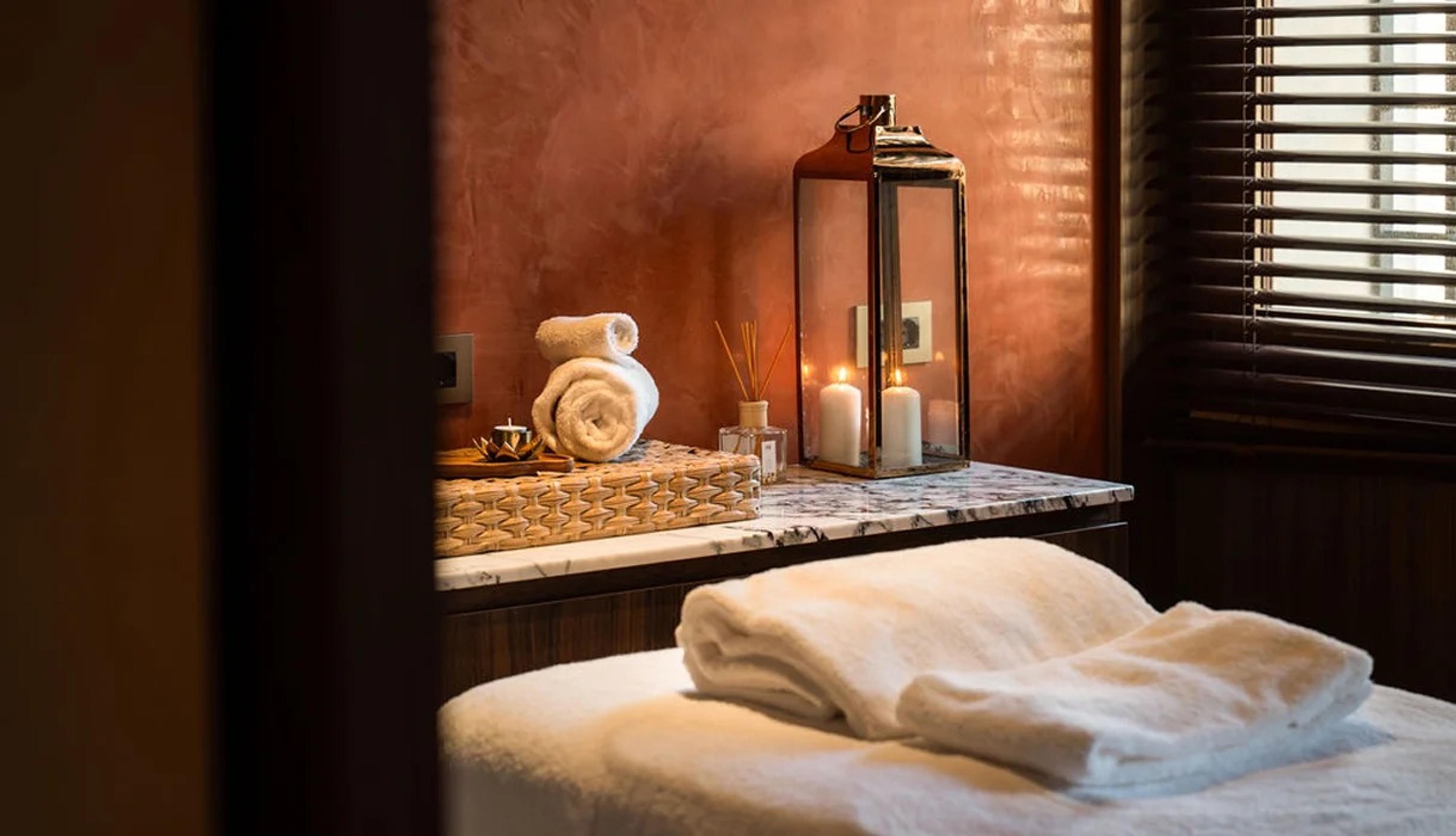 Rolled white towels and lit candles on a marble table in a treatment room, with a folded towel on the table in the foreground.