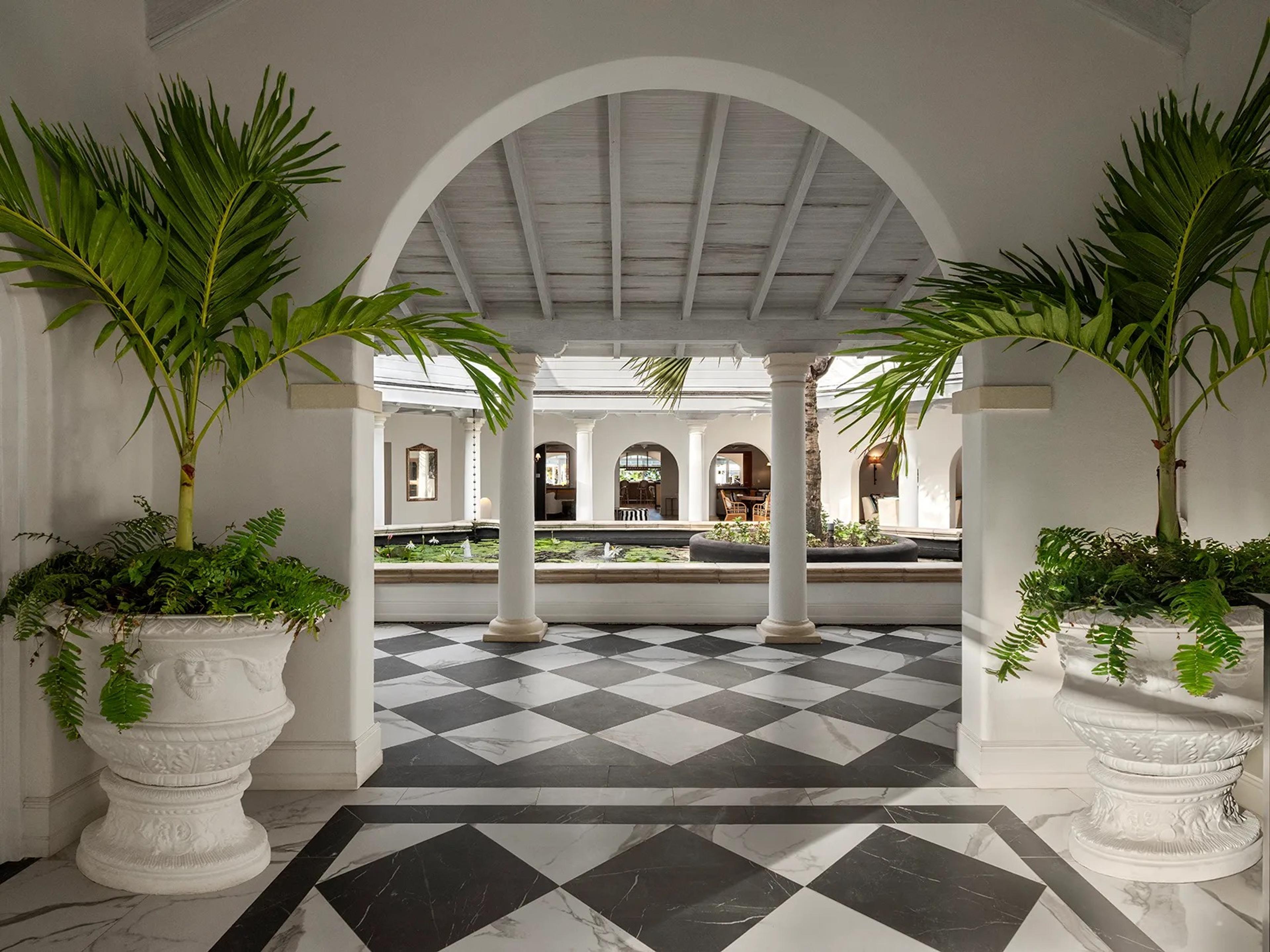An arched lobby with a black-and-white chequered floor and potted palms in white urns