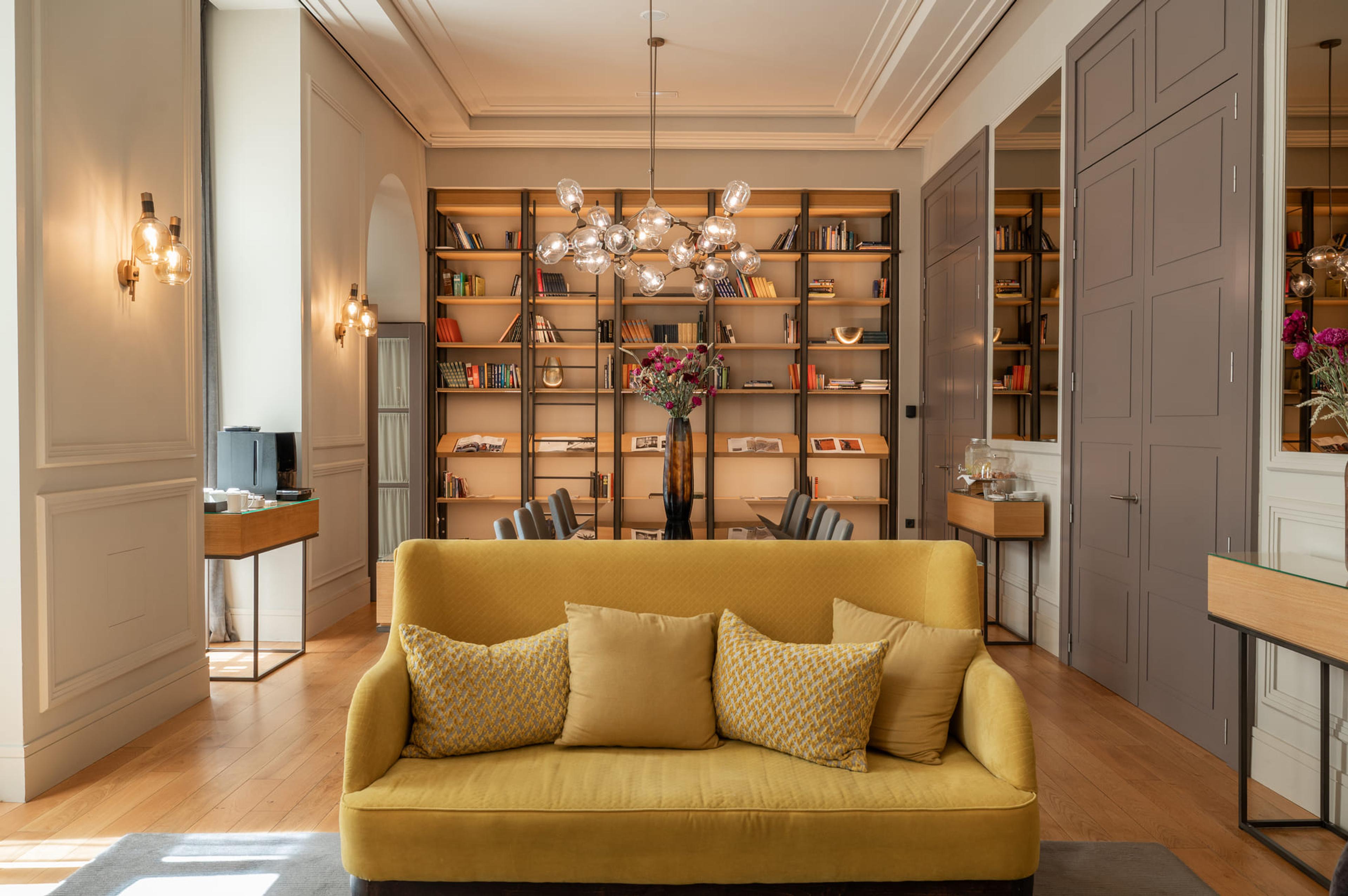 A mustard-yellow sofa in front of tall bookshelves, under a cluster of glass globe lights, in a room with pale panelled walls and a wooden floor.