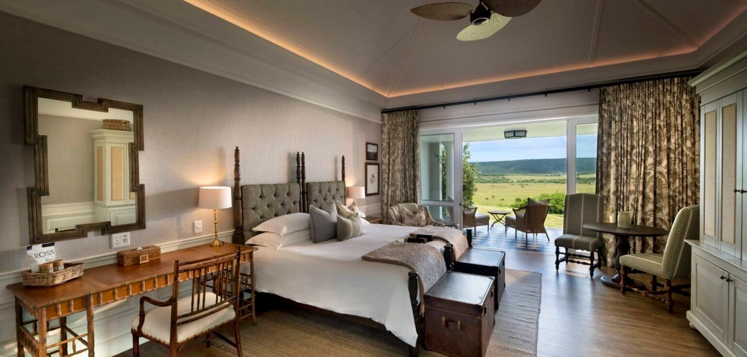 A four-poster king bed facing a seating area, with glass doors open to a terrace and hill views.