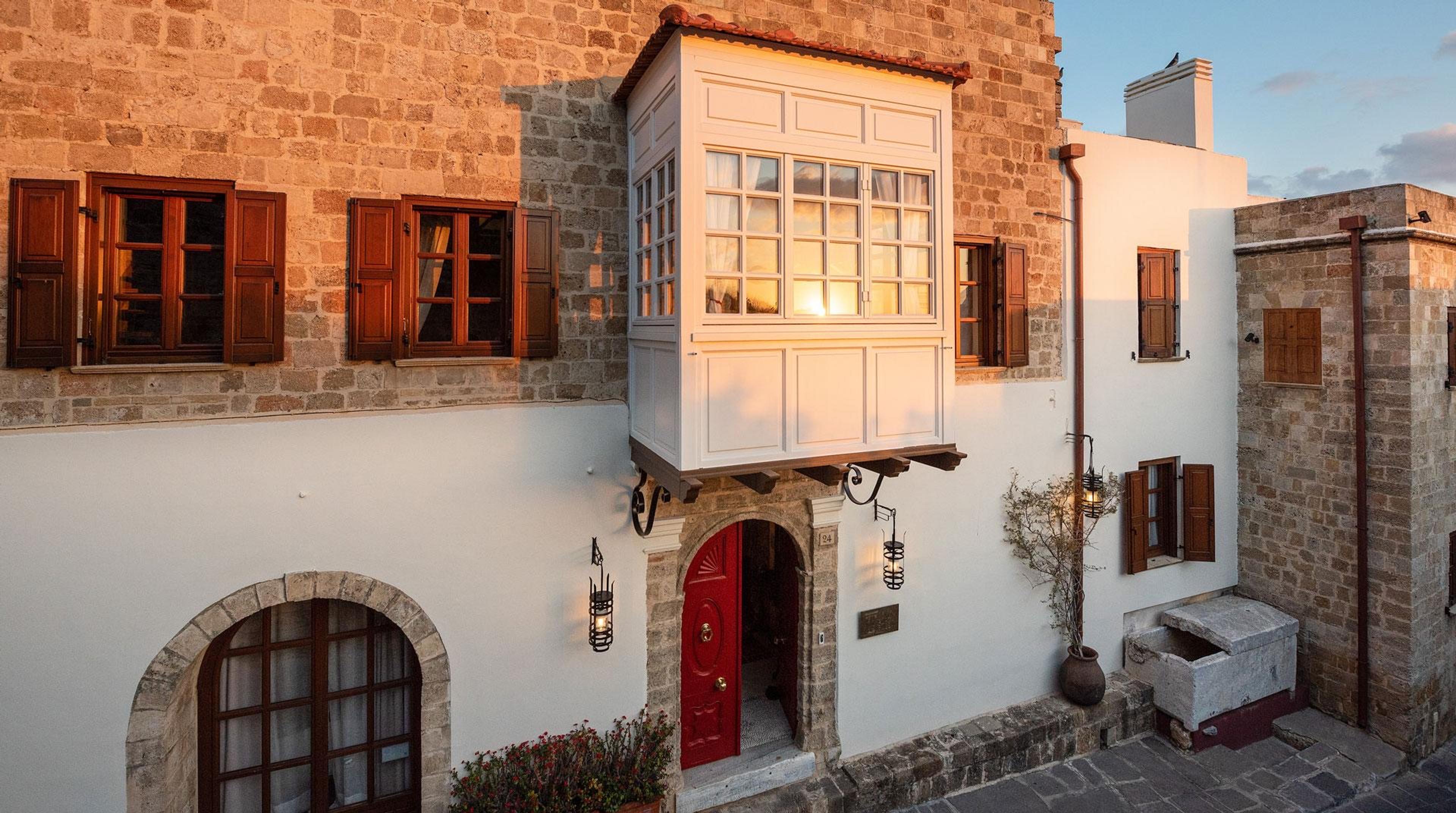 A white building with a red front door and an overhanging timber bay window, photographed at dusk.