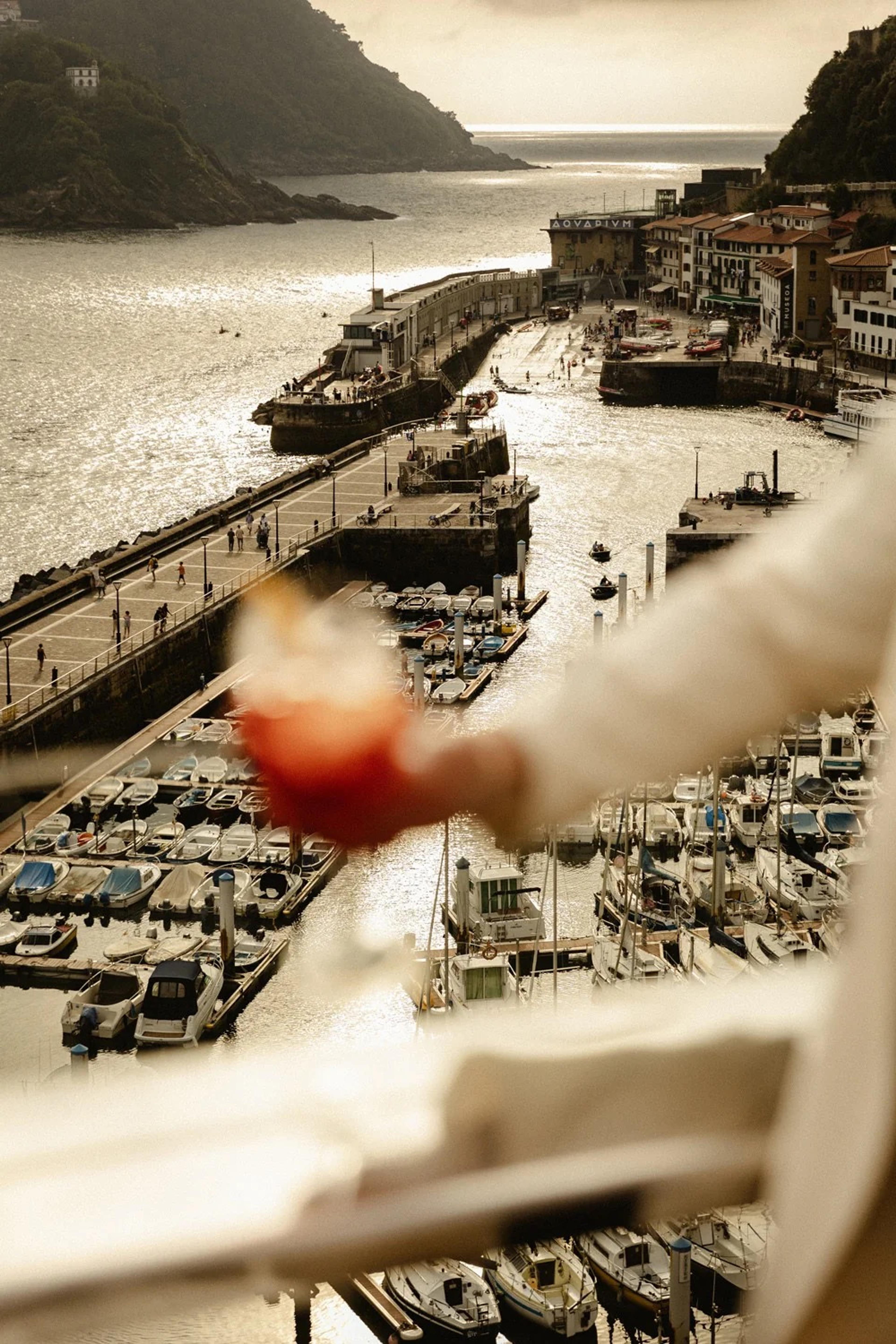 An aerial view over a marina crowded with small boats and a stone jetty, with a blurred arm and a piece of fruit in the foreground.