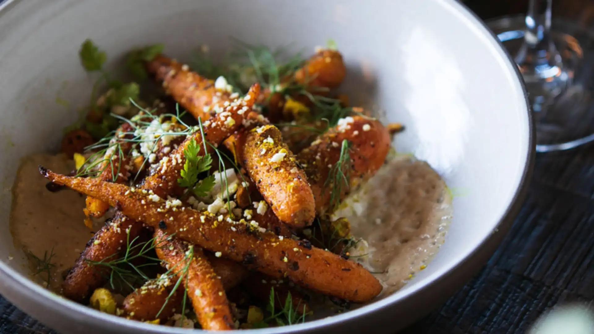 Roasted carrots with crumbled cheese and herbs in a white bowl, resting on a smear of pale puree.