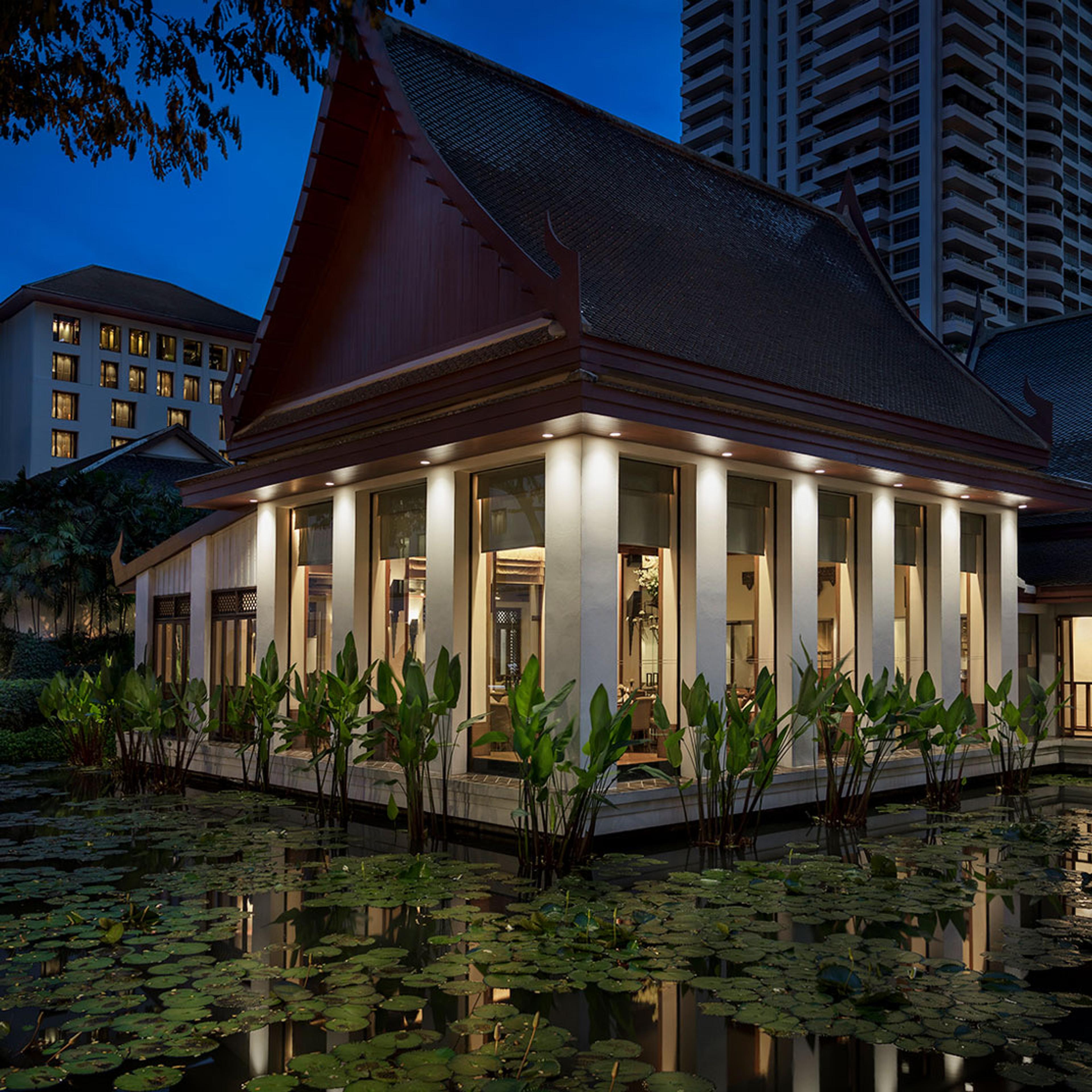 A lantern-lit pavilion at dusk among trees