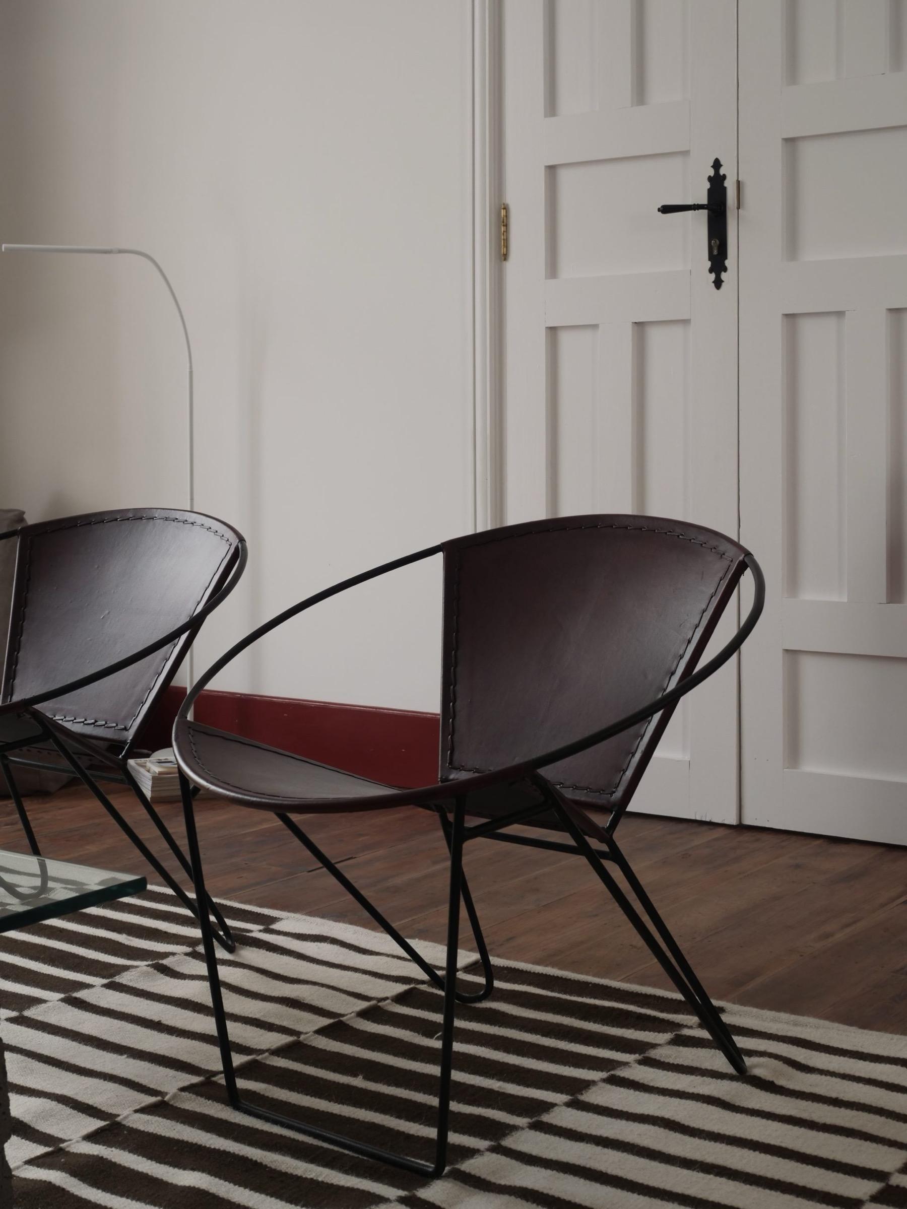 Two round-backed leather armchairs on a black and white striped rug, facing a panelled white door, with a floor lamp beside them.