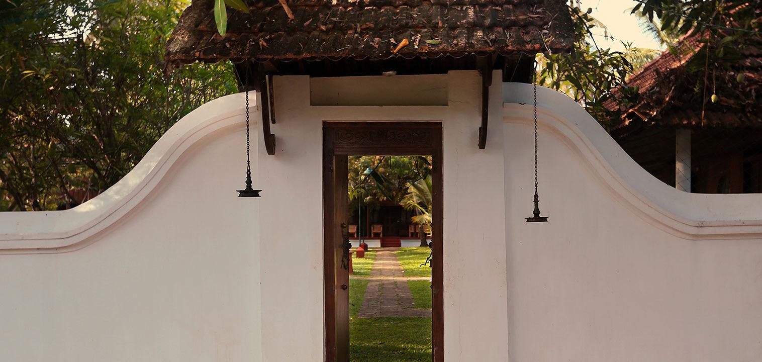 An open gateway in a white wall under a tiled roof, leading to a lawn and buildings beyond