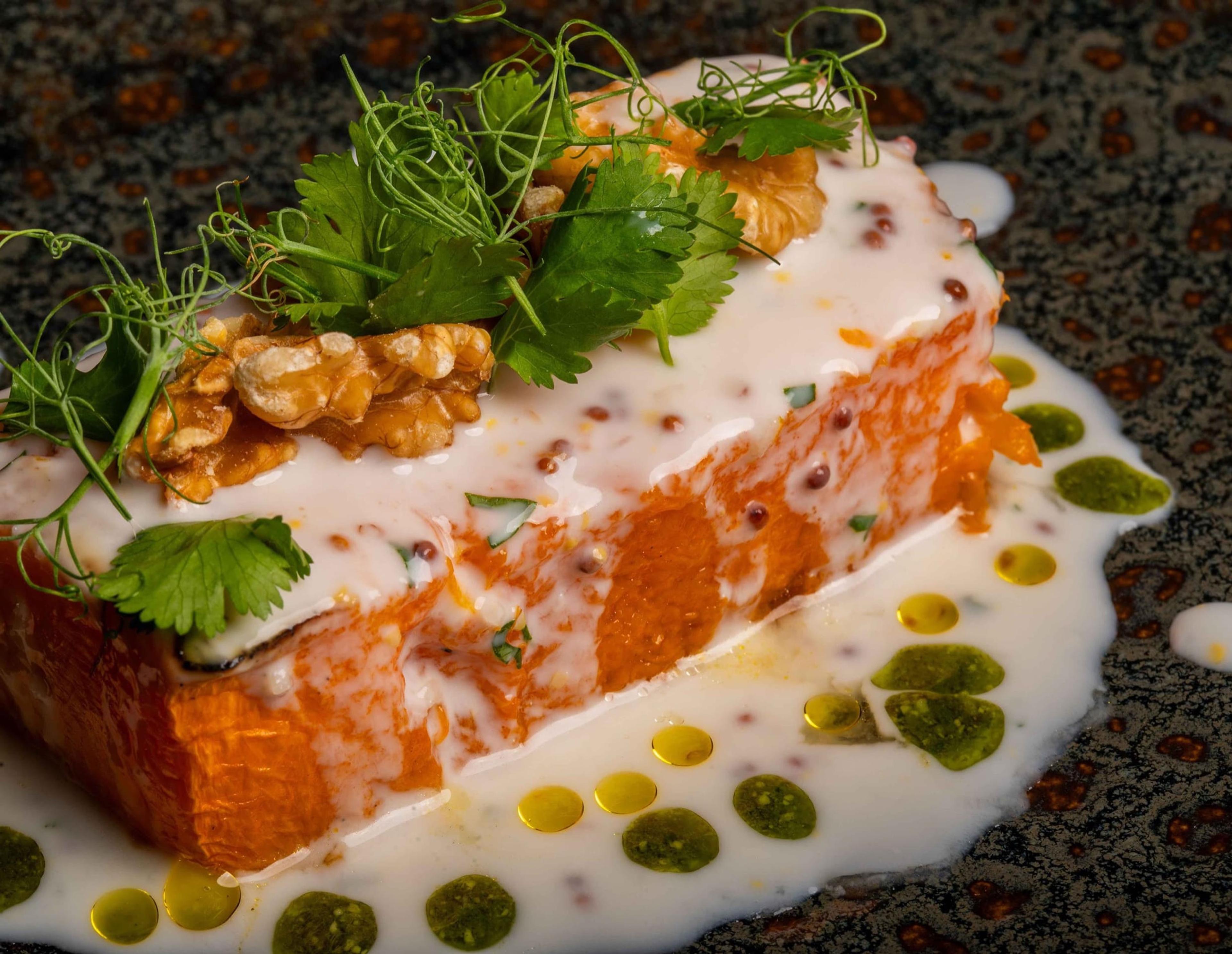 A layered fish dish topped with fresh herbs, dressed with green oil