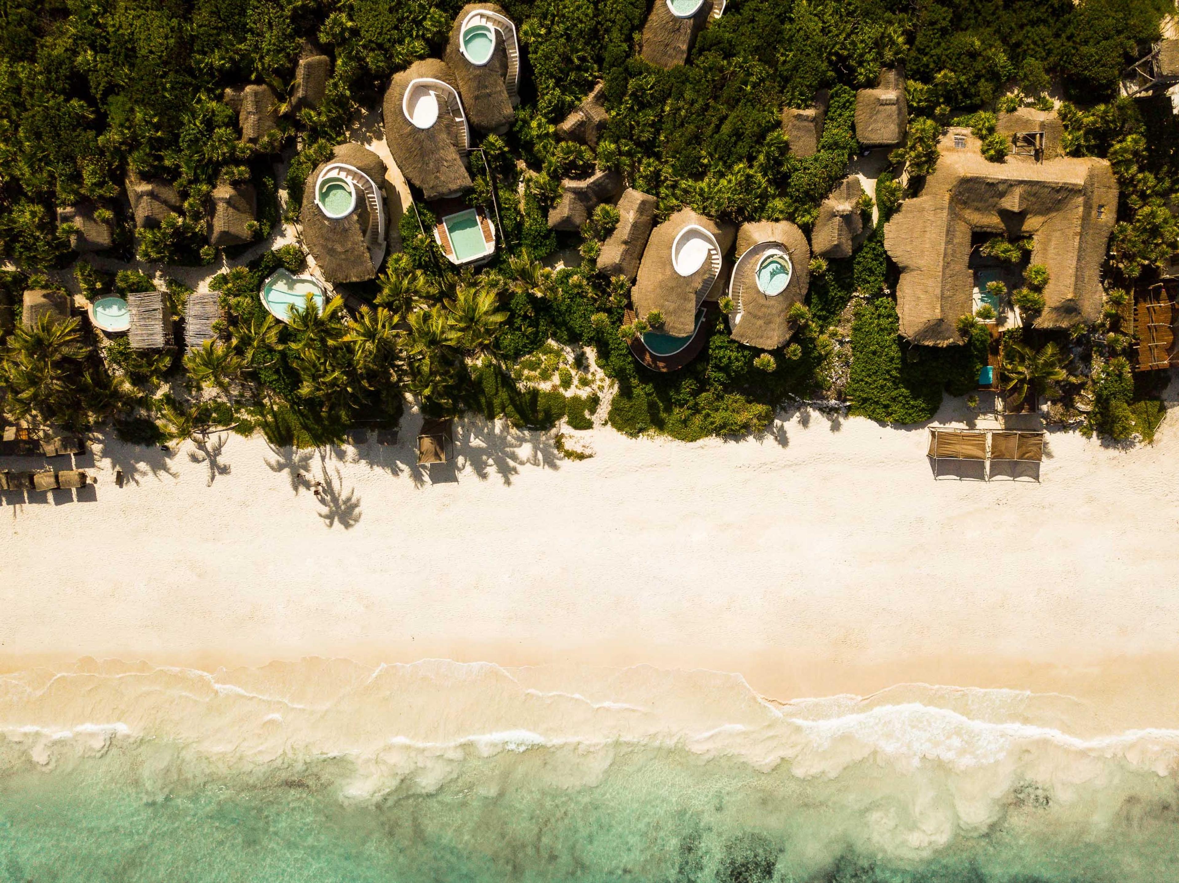 an aerial view of round thatched-roof villas with private plunge pools set closely among palm trees and jungle canopy