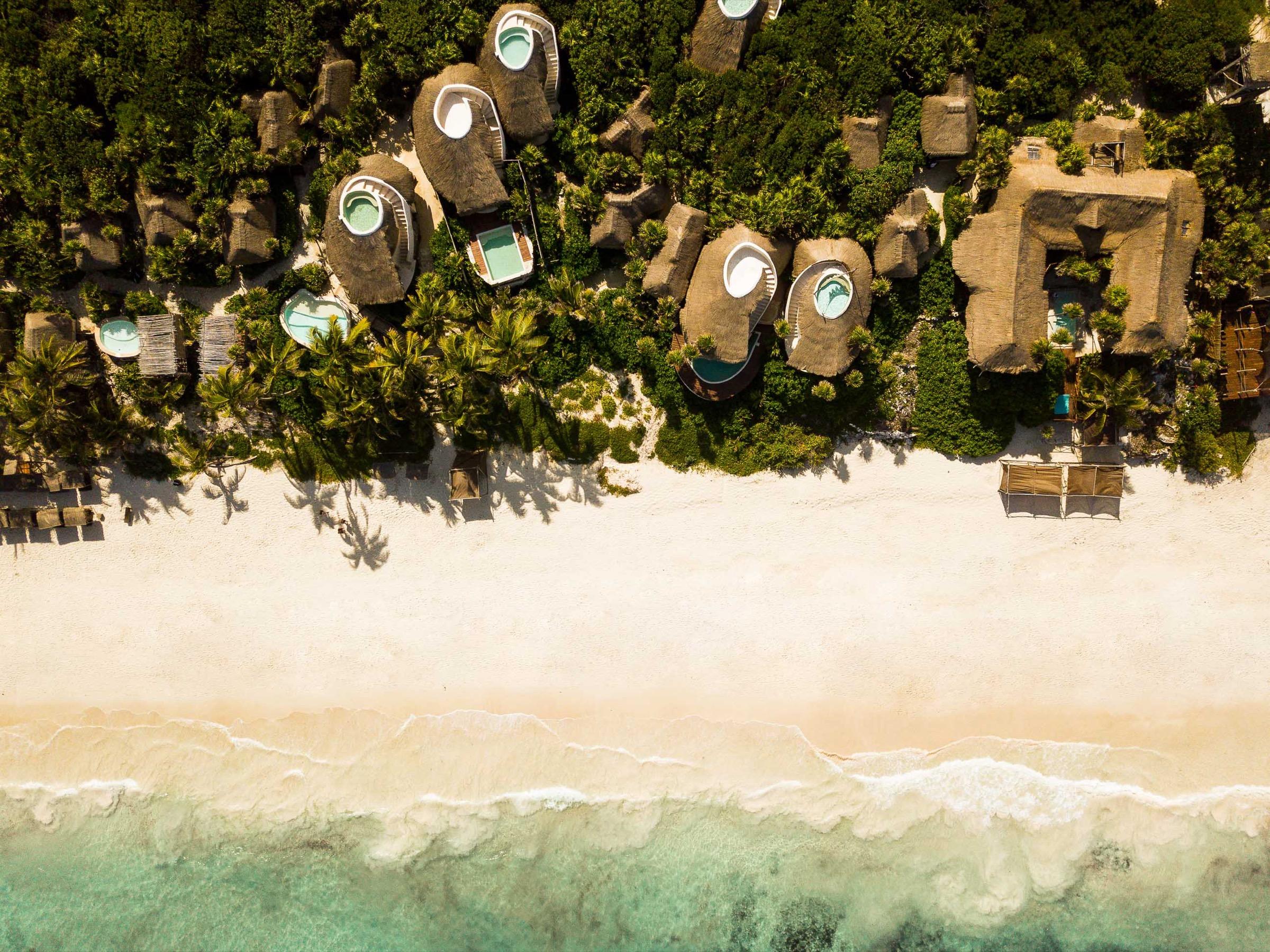an aerial view of round thatched-roof villas with private plunge pools set closely among palm trees and jungle canopy