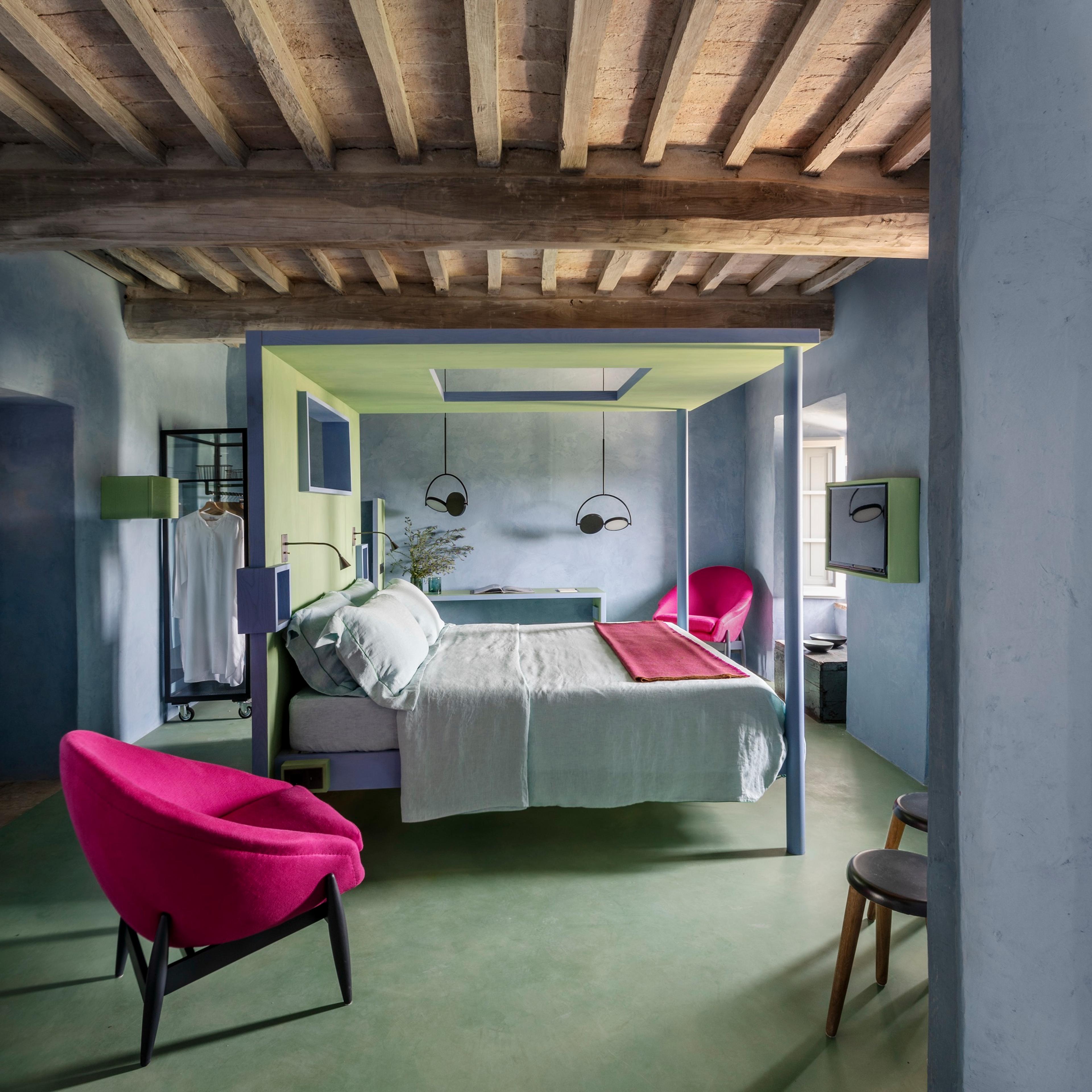 A bedroom with a lime green and grey four poster frame, a pink armchair, a wood beamed ceiling and a green floor.