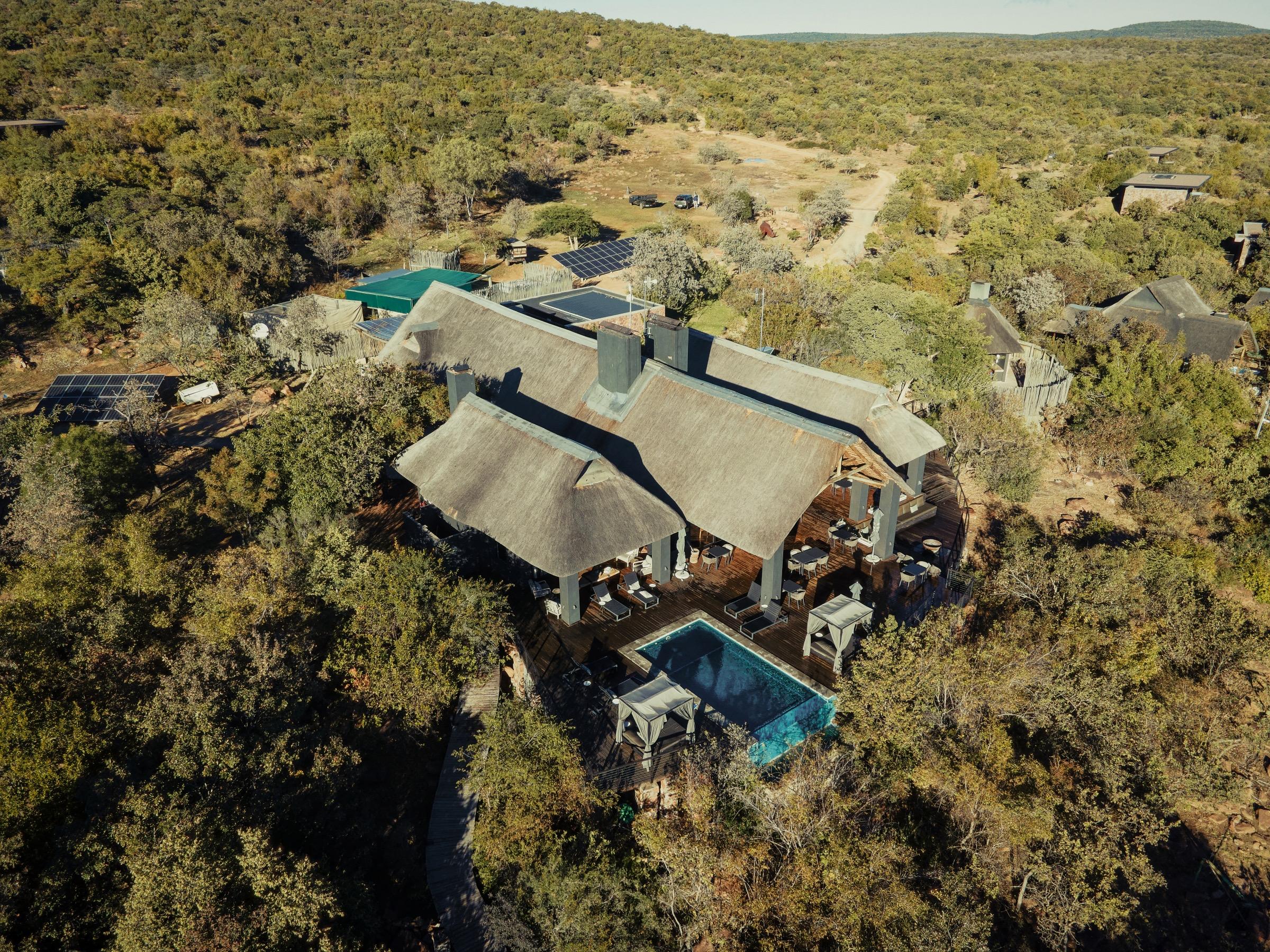 An aerial view of the main lodge's thatched roof and shaded dining deck beside a bright turquoise plunge pool with loungers around it.