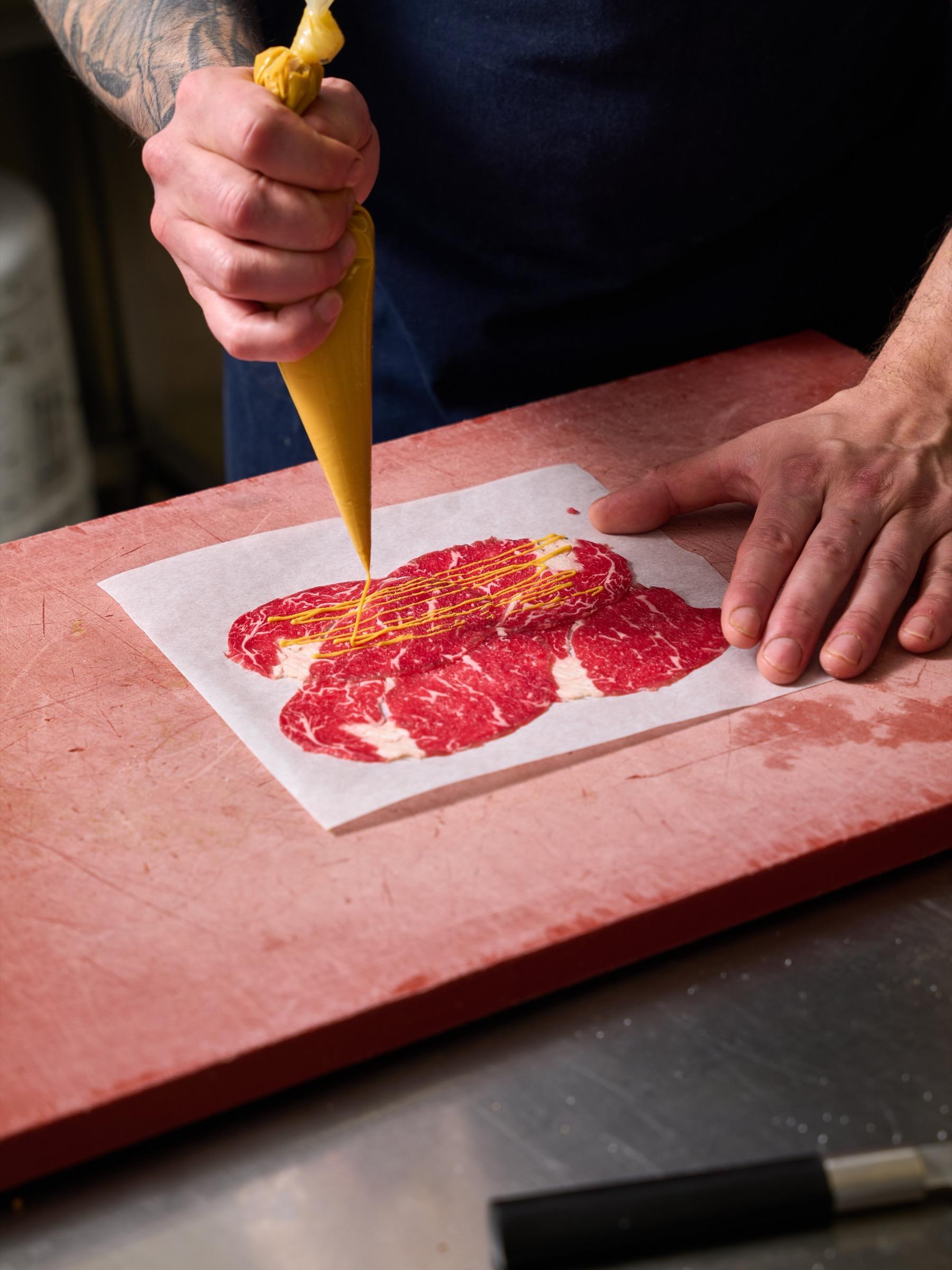 Slices of cured meat being dressed on a pink board