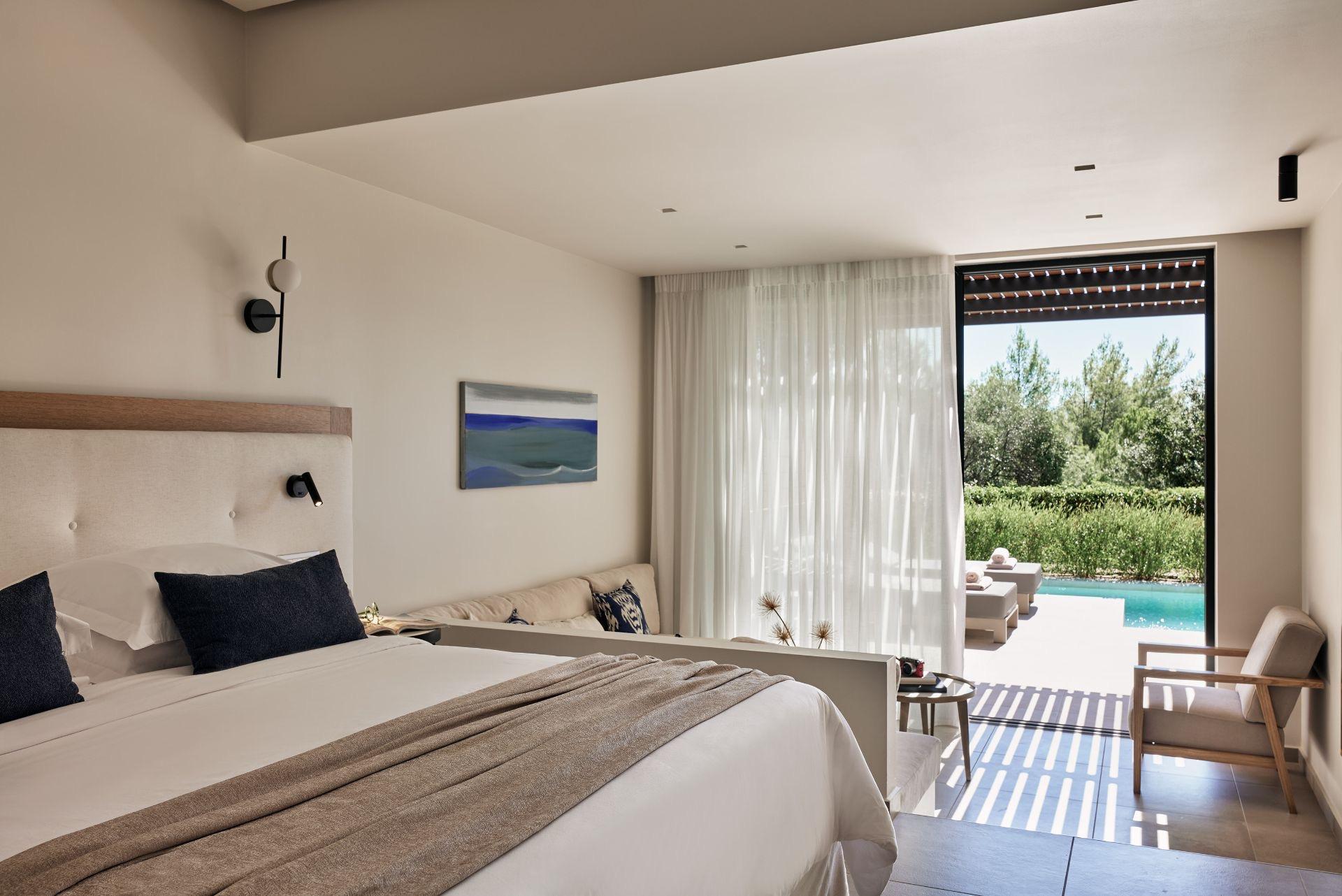 A hotel bedroom with a made bed and a painting on the wall, its sliding doors open to a terrace and pool beyond.