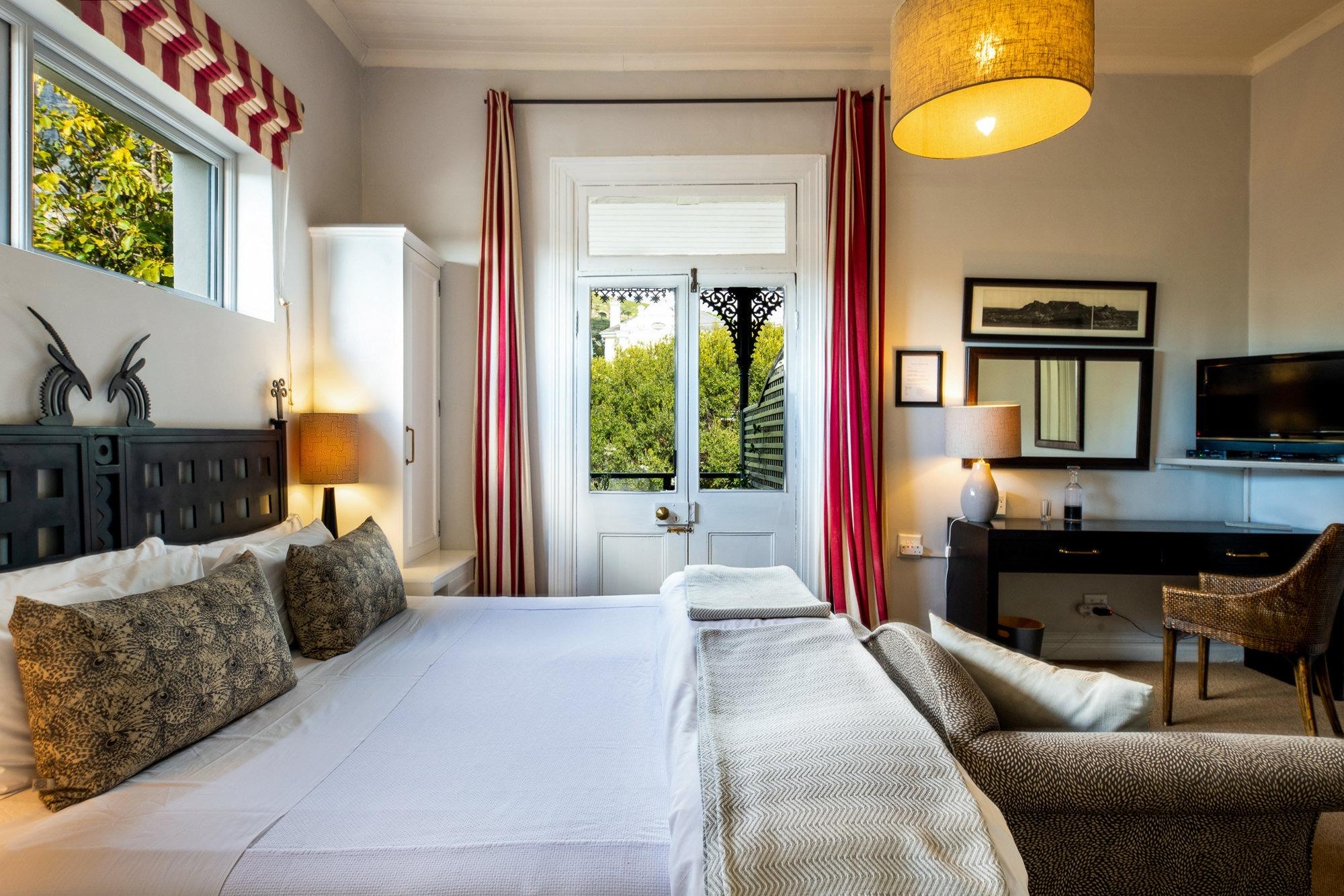 a bedroom with a dark carved headboard topped with antelope finials, red striped curtains, and a stained glass door open to a balcony