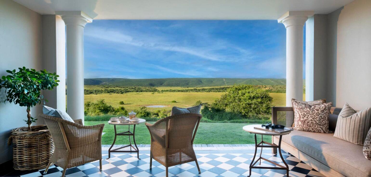 Wicker armchairs and a sofa on a checkered verandah, looking out over open grassland to the hills.