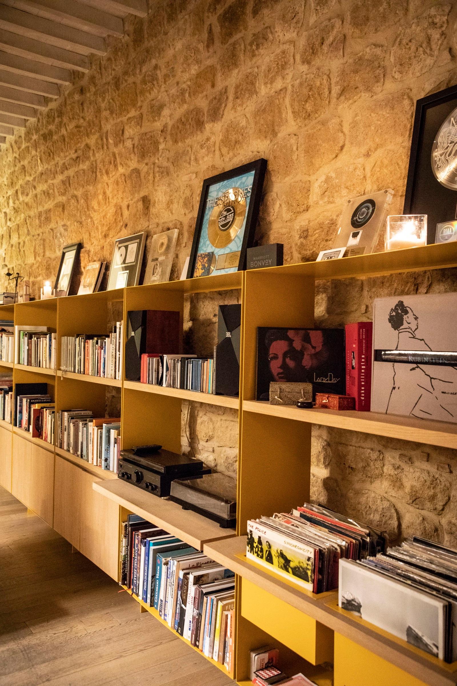 Floor-to-ceiling wooden shelving against a stone wall, holding books, framed records and a turntable.
