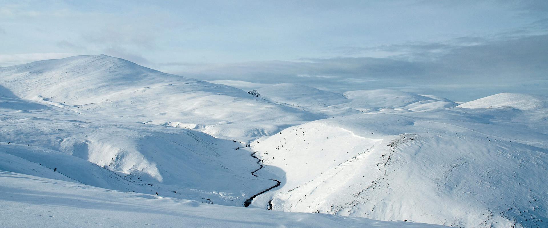 Snow covered hills and a frozen burn seen from a high vantage point under a pale winter sky.