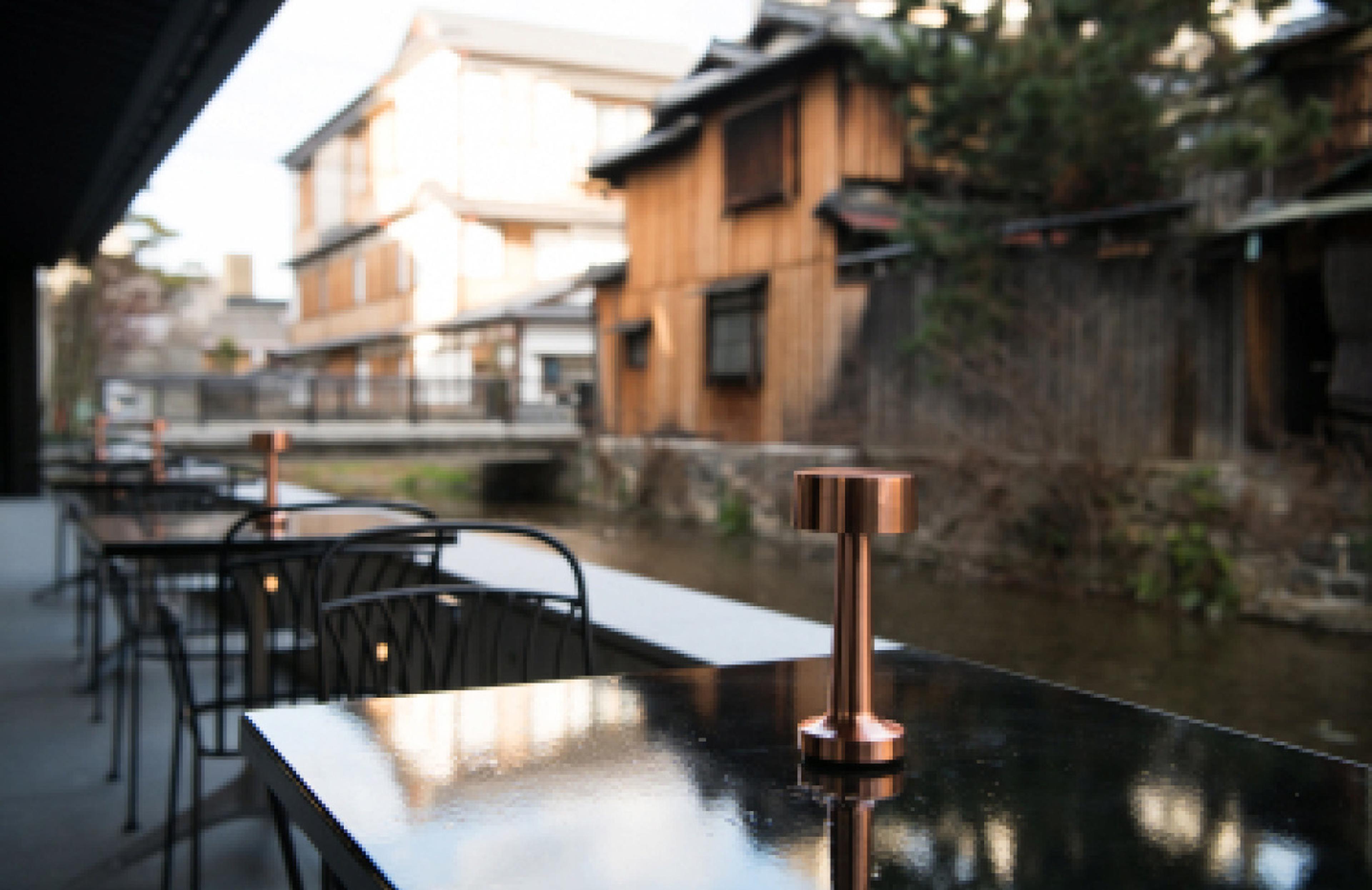 outdoor dining tables along a canal in daylight, with traditional wooden houses on the opposite bank