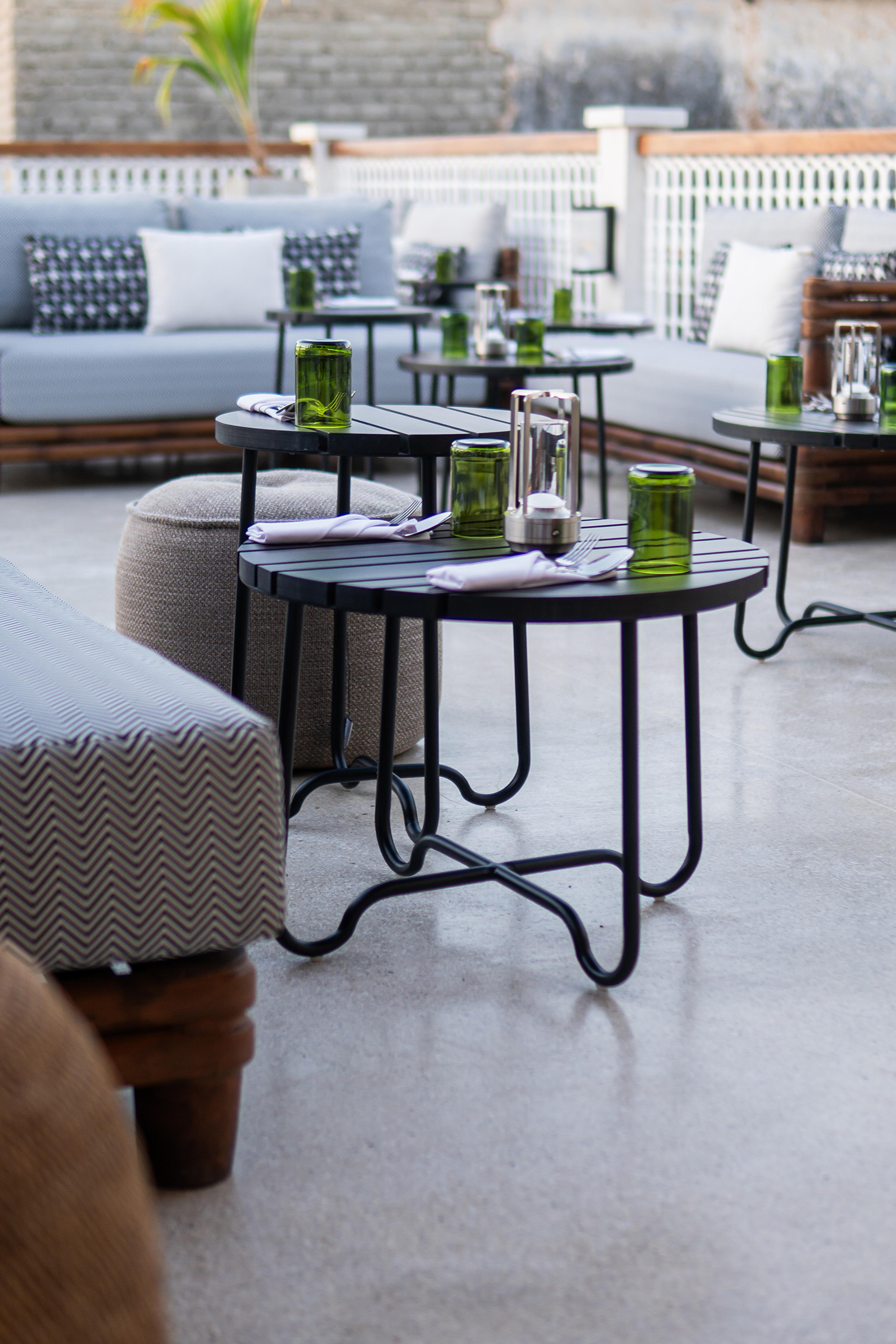 Grey upholstered sofas and low black tables with lanterns are arranged on an outdoor terrace.
