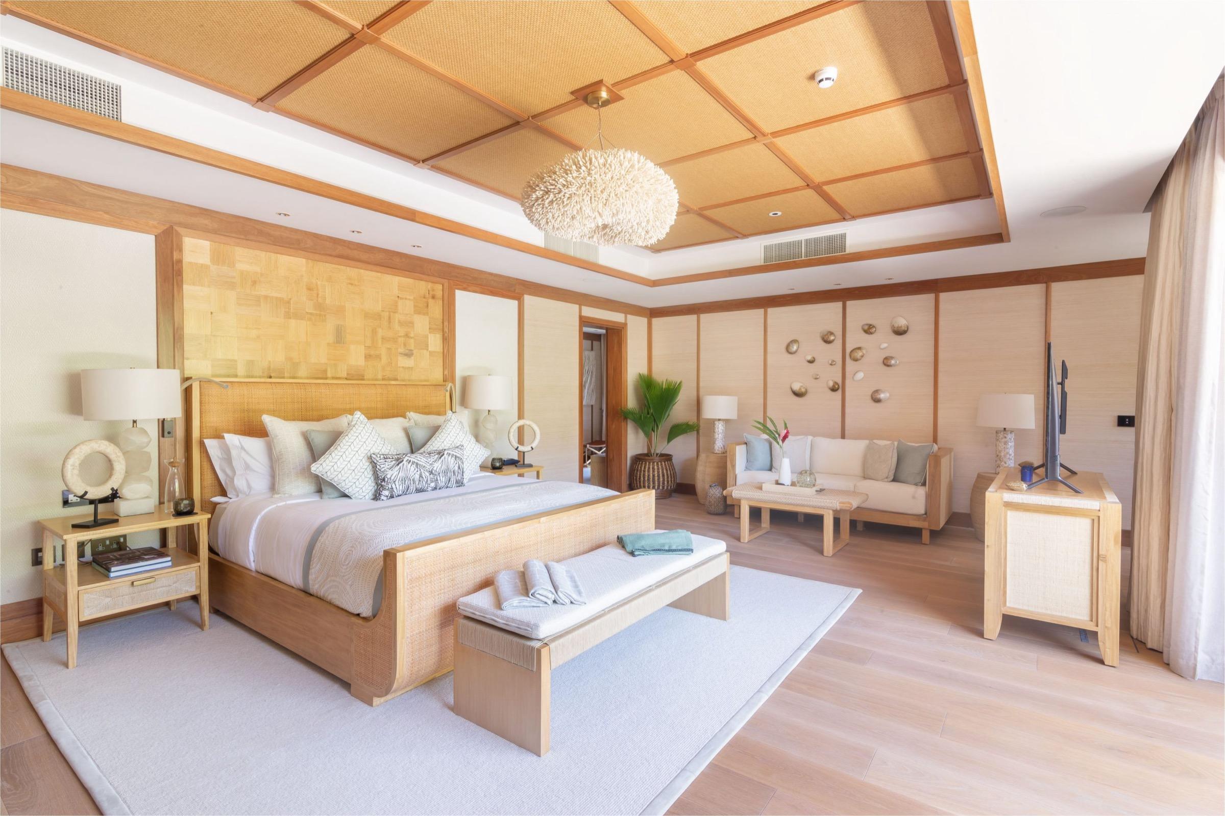 A spacious bedroom with a woven headboard, a shell-shaped pendant light, and a separate seating area with a sofa.
