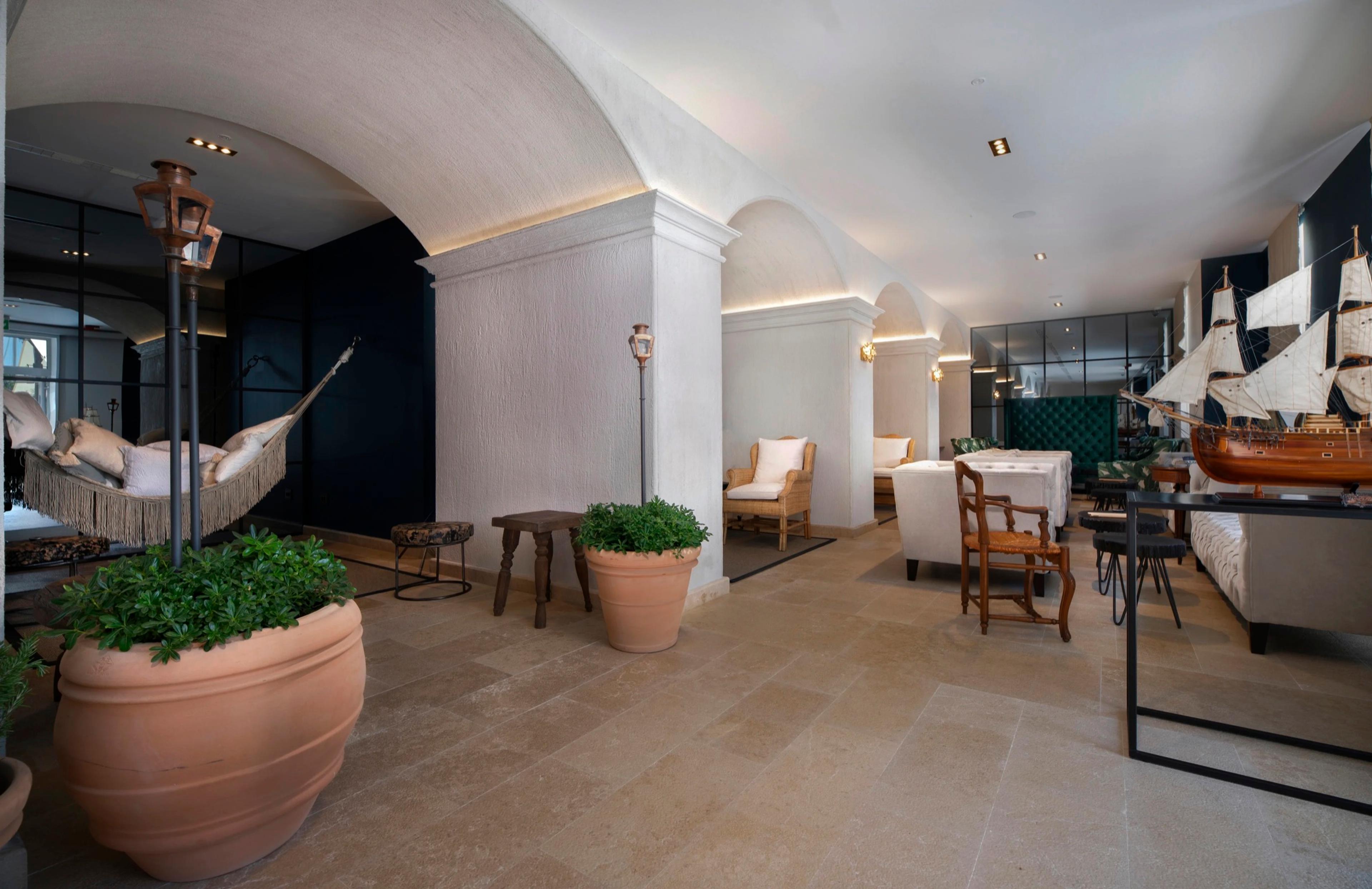 A hotel lobby with arched ceilings, a hammock hung between posts, terracotta planters, and a model sailing ship on a table.
