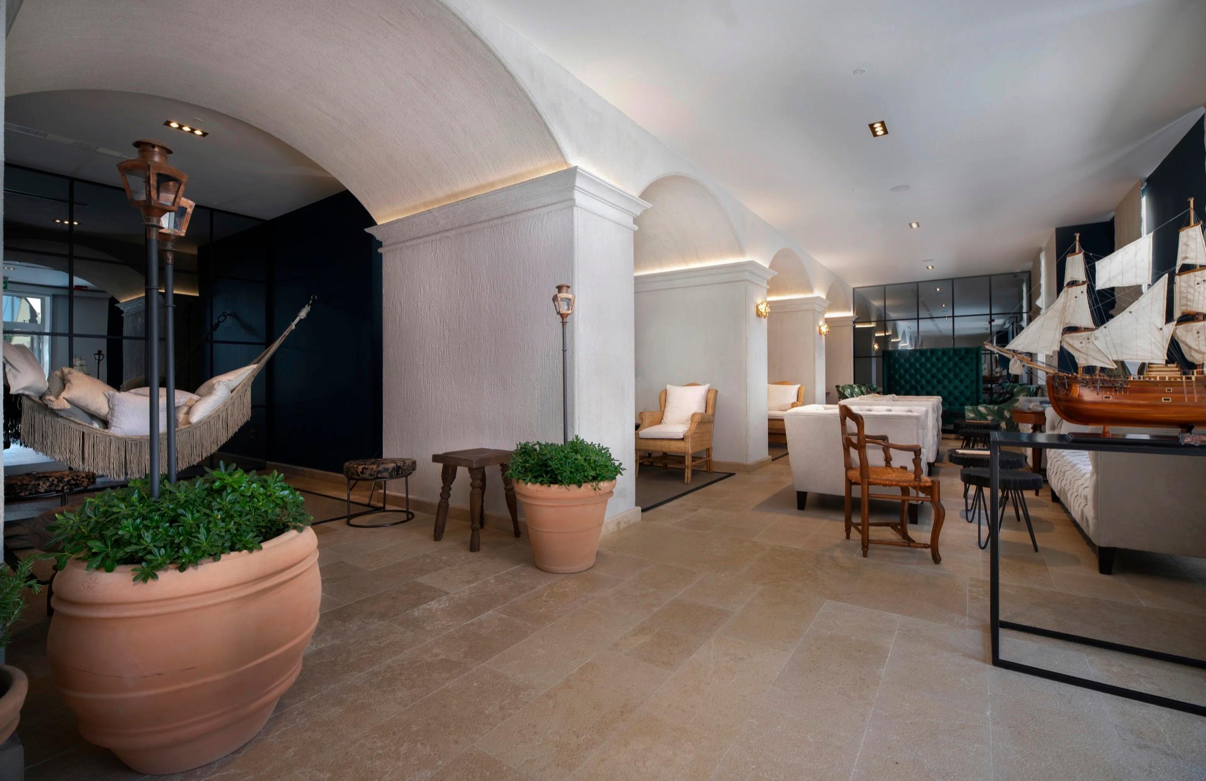 A hotel lobby with arched ceilings, a hammock hung between posts, terracotta planters, and a model sailing ship on a table.