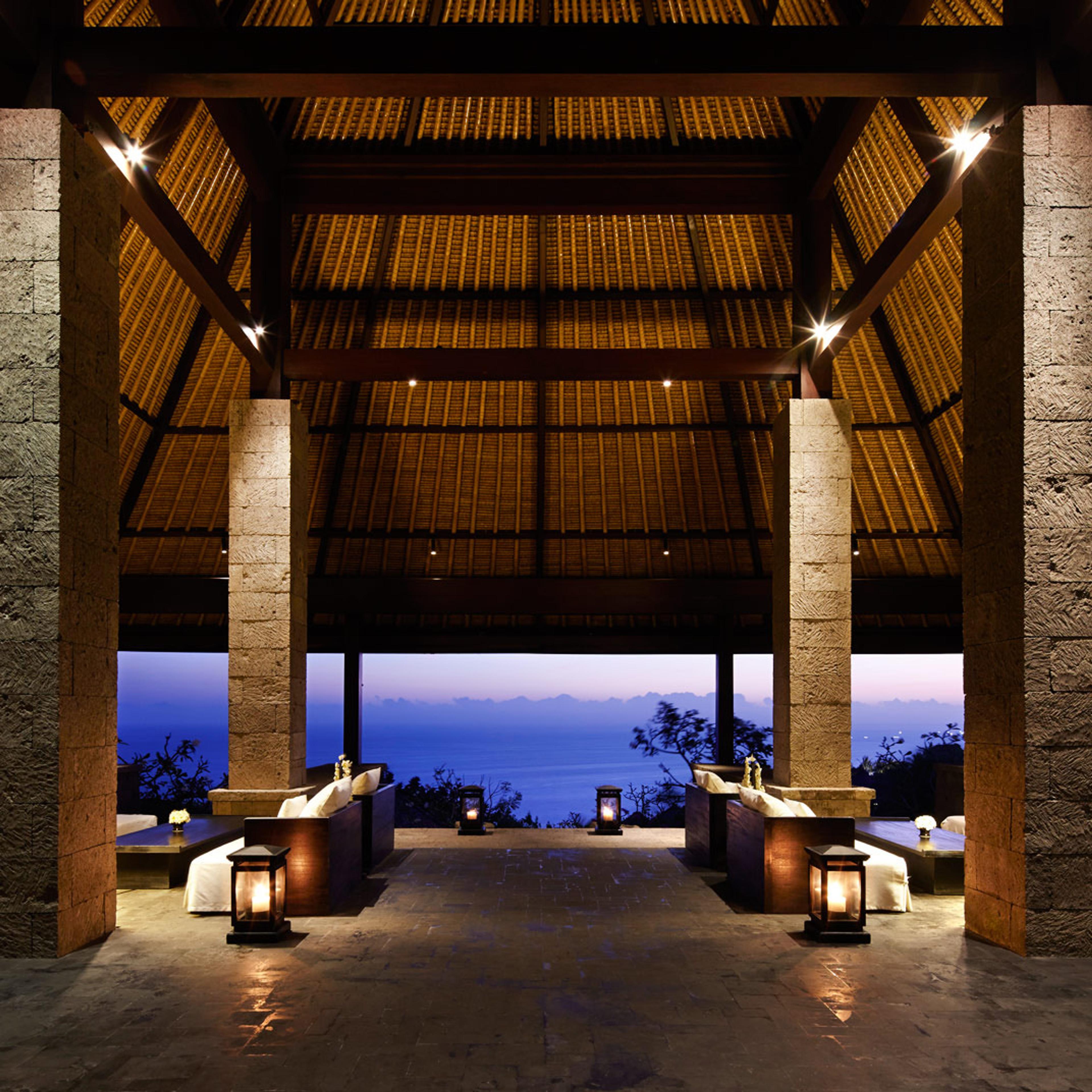 An open pavilion lounge between stone columns, looking out over the ocean at dusk