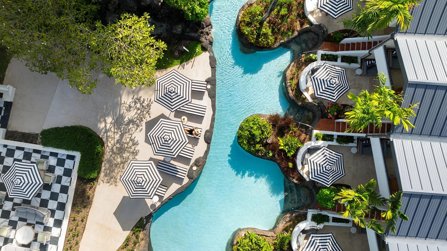 A curving pool between rooms and striped umbrellas, seen from directly above