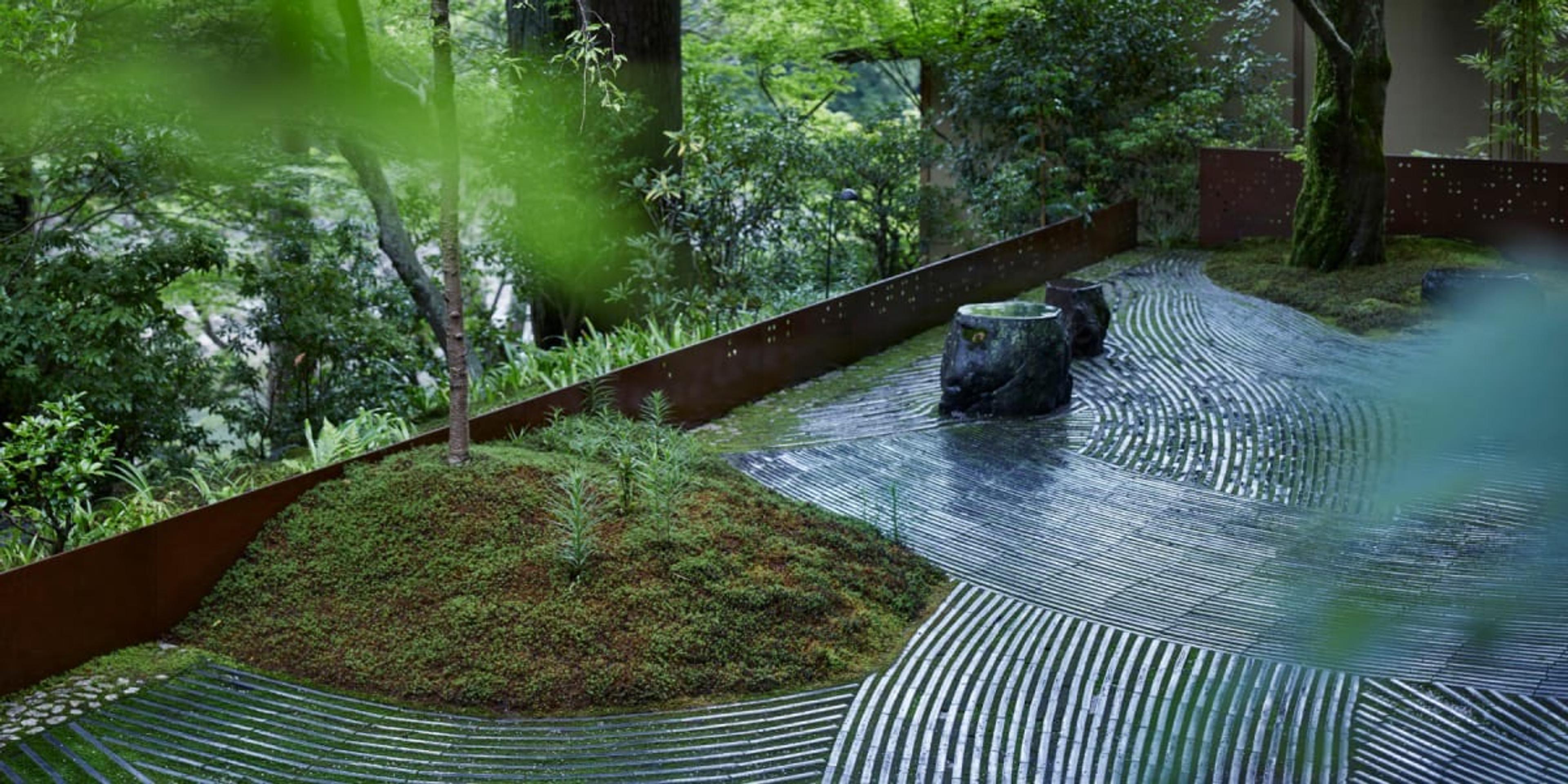 A raked gravel garden with moss, a single stone and a low wall, under trees