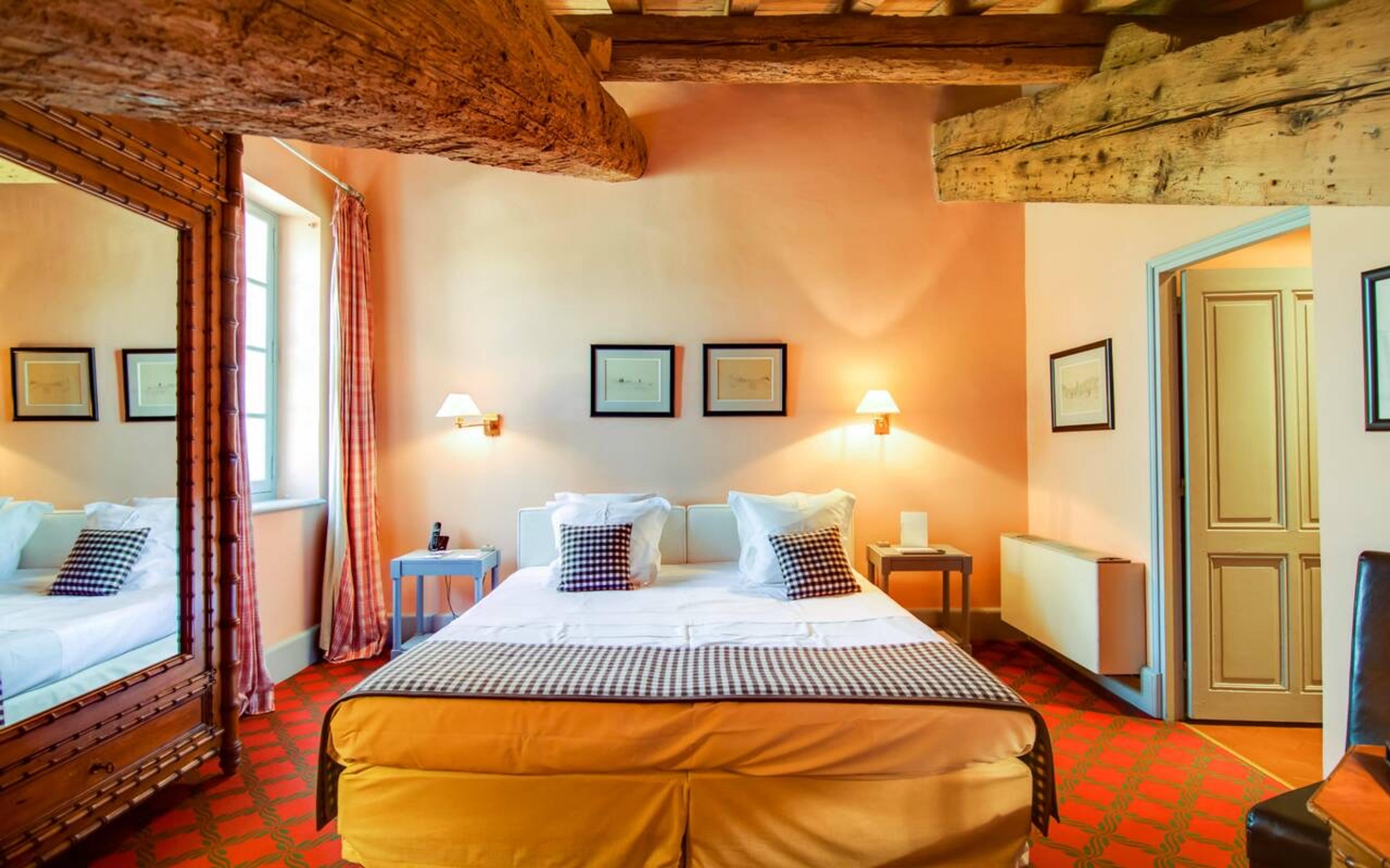 A bed with checked cushions under wooden ceiling beams, in a room with terracotta-orange walls and striped curtains.