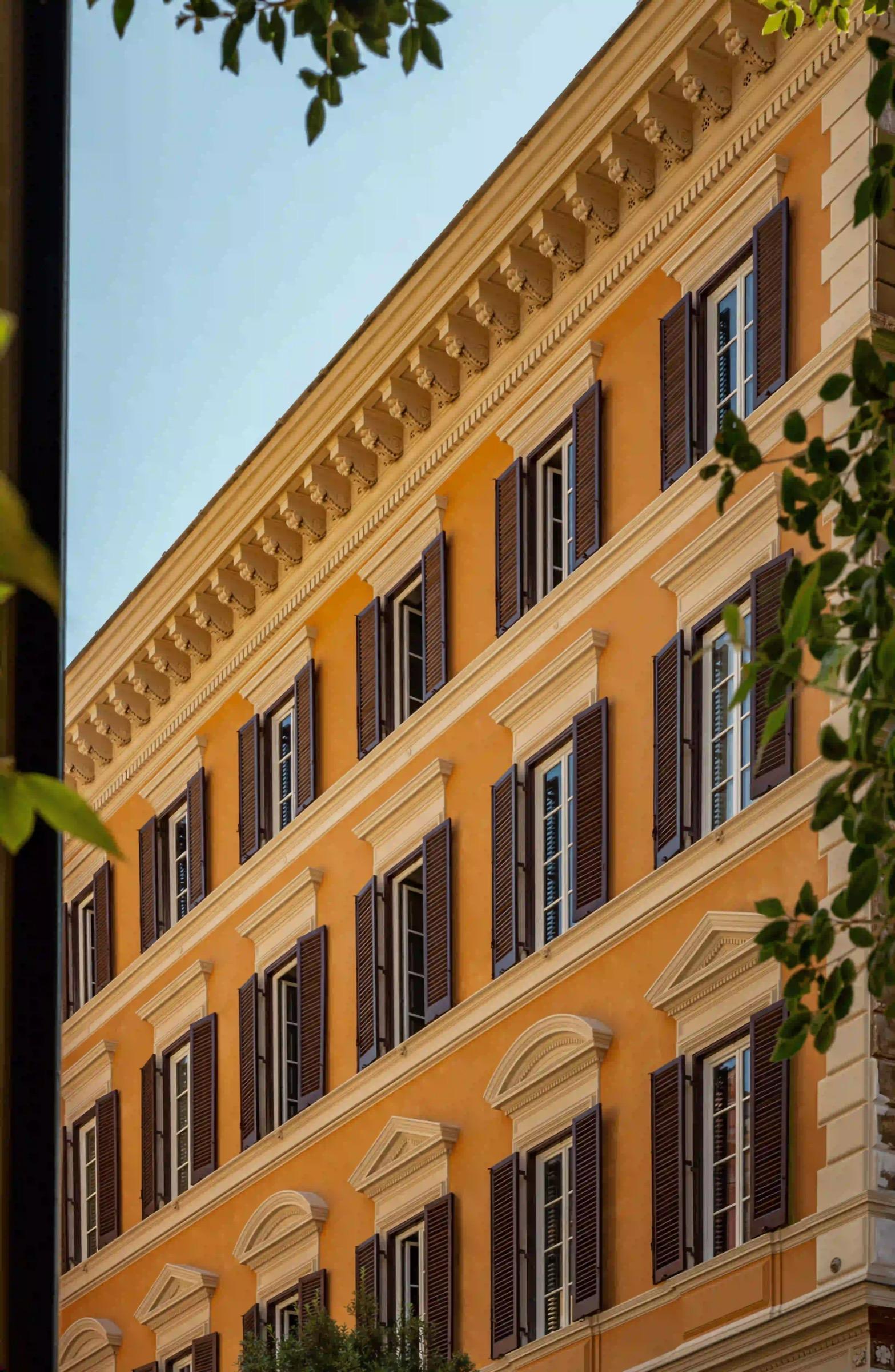 An orange building facade with rows of symmetrical windows and dark shutters under a clear sky.
