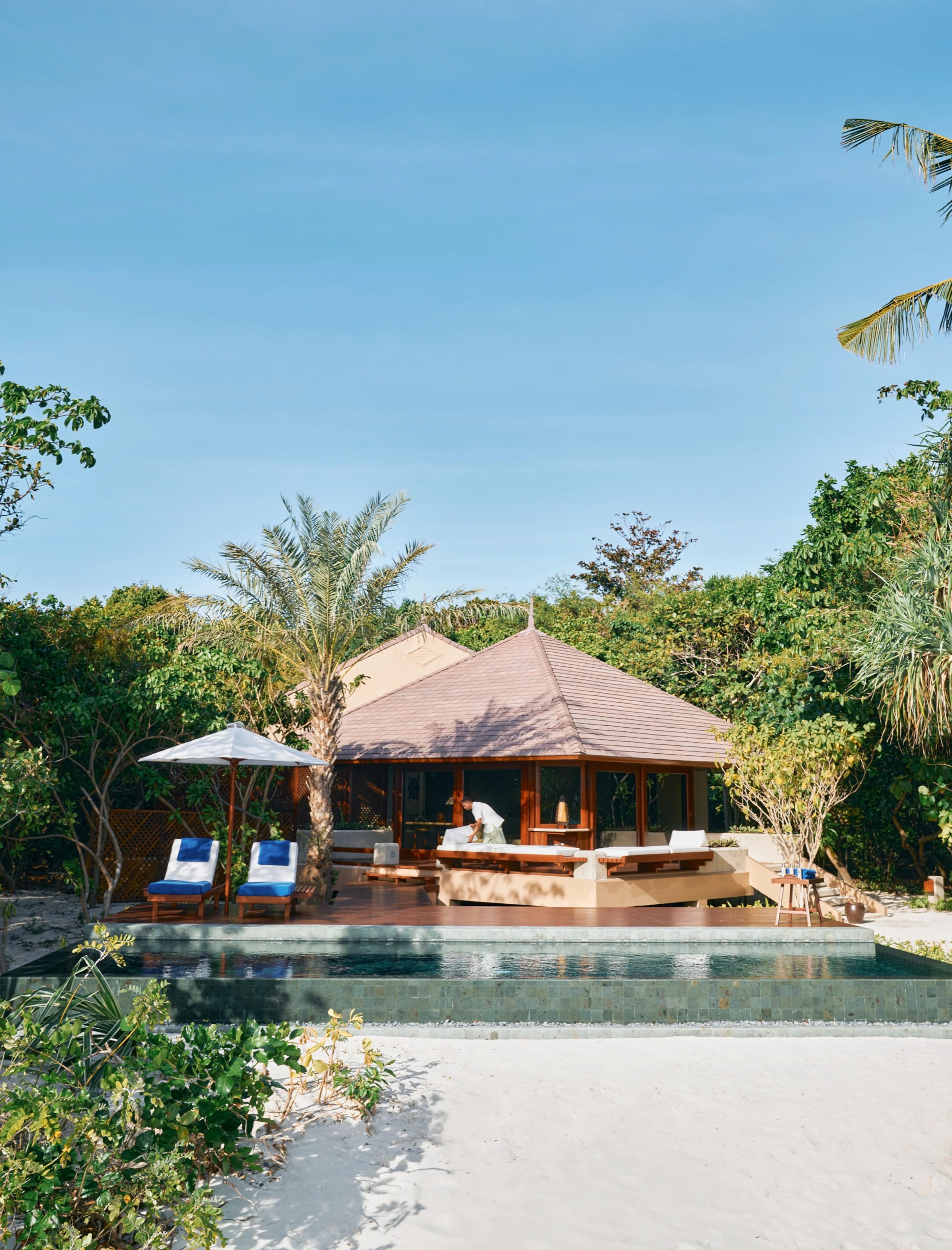 A thatched roof casita with its own plunge pool and sun loungers, set among trees at the edge of a white sand beach.