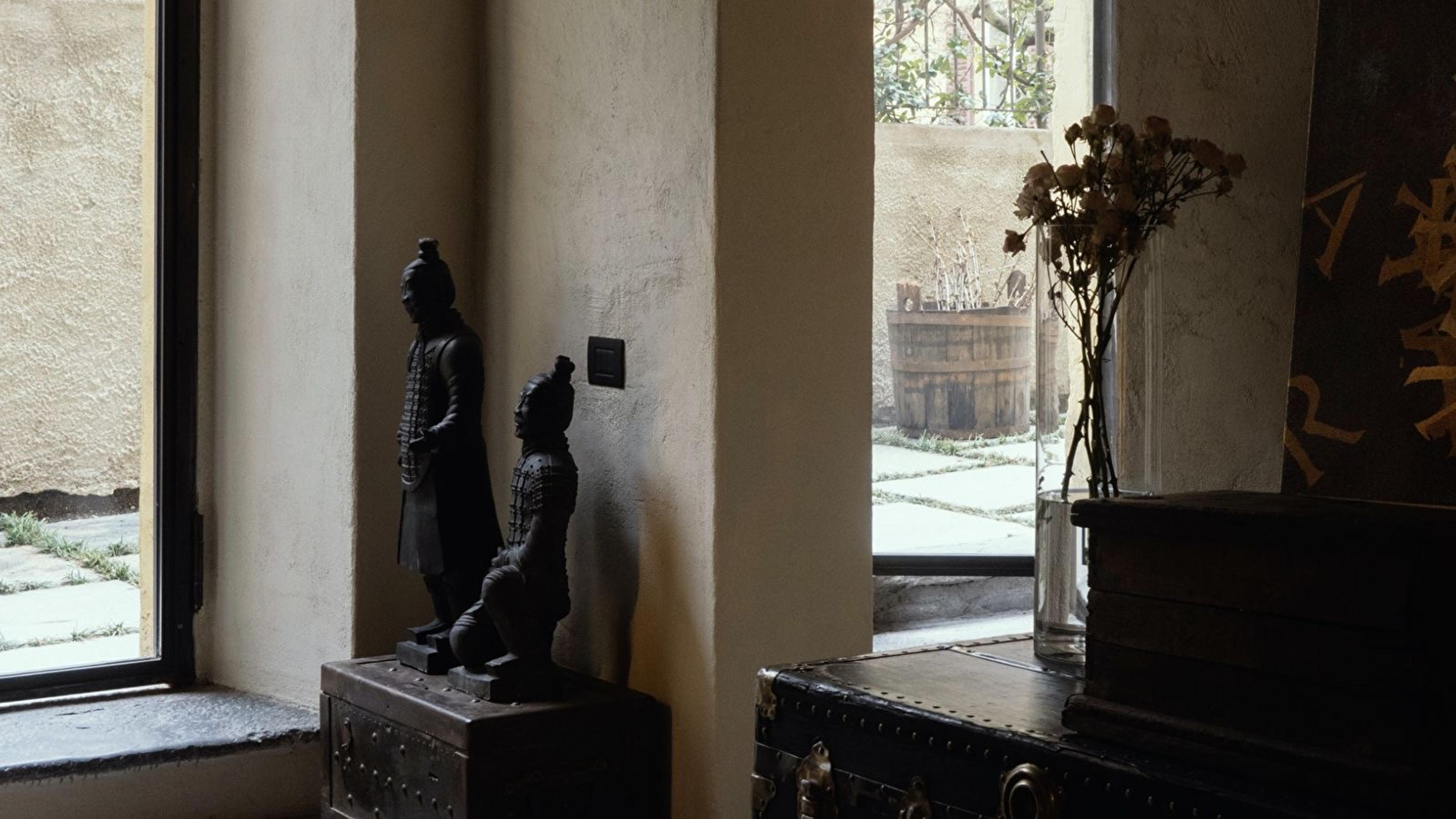 small terracotta warrior statues on a window sill, looking out through another window onto a courtyard