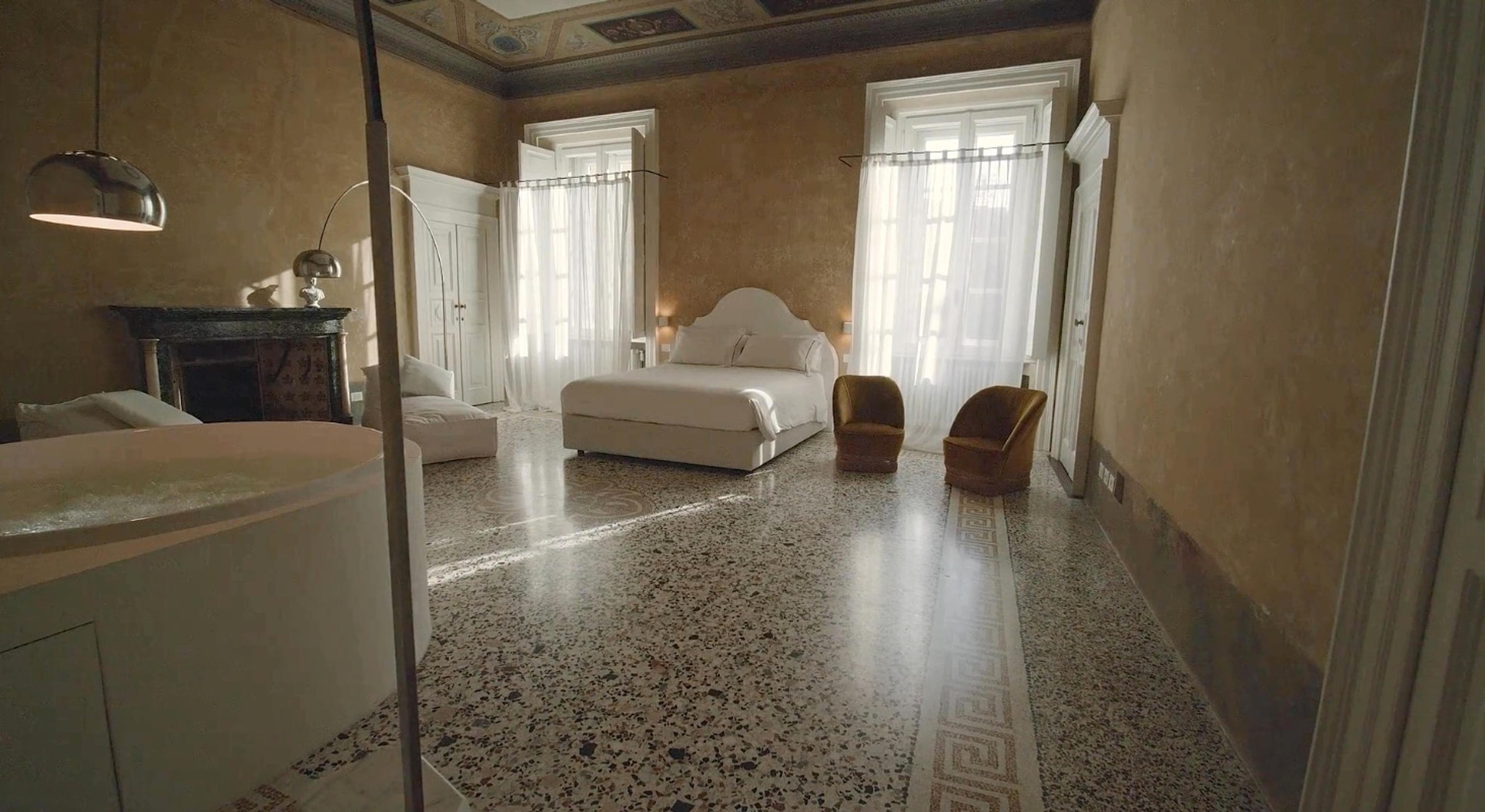 a frescoed bedroom with a freestanding bathtub, a canopy bed, a terrazzo floor and tall shuttered windows letting in daylight