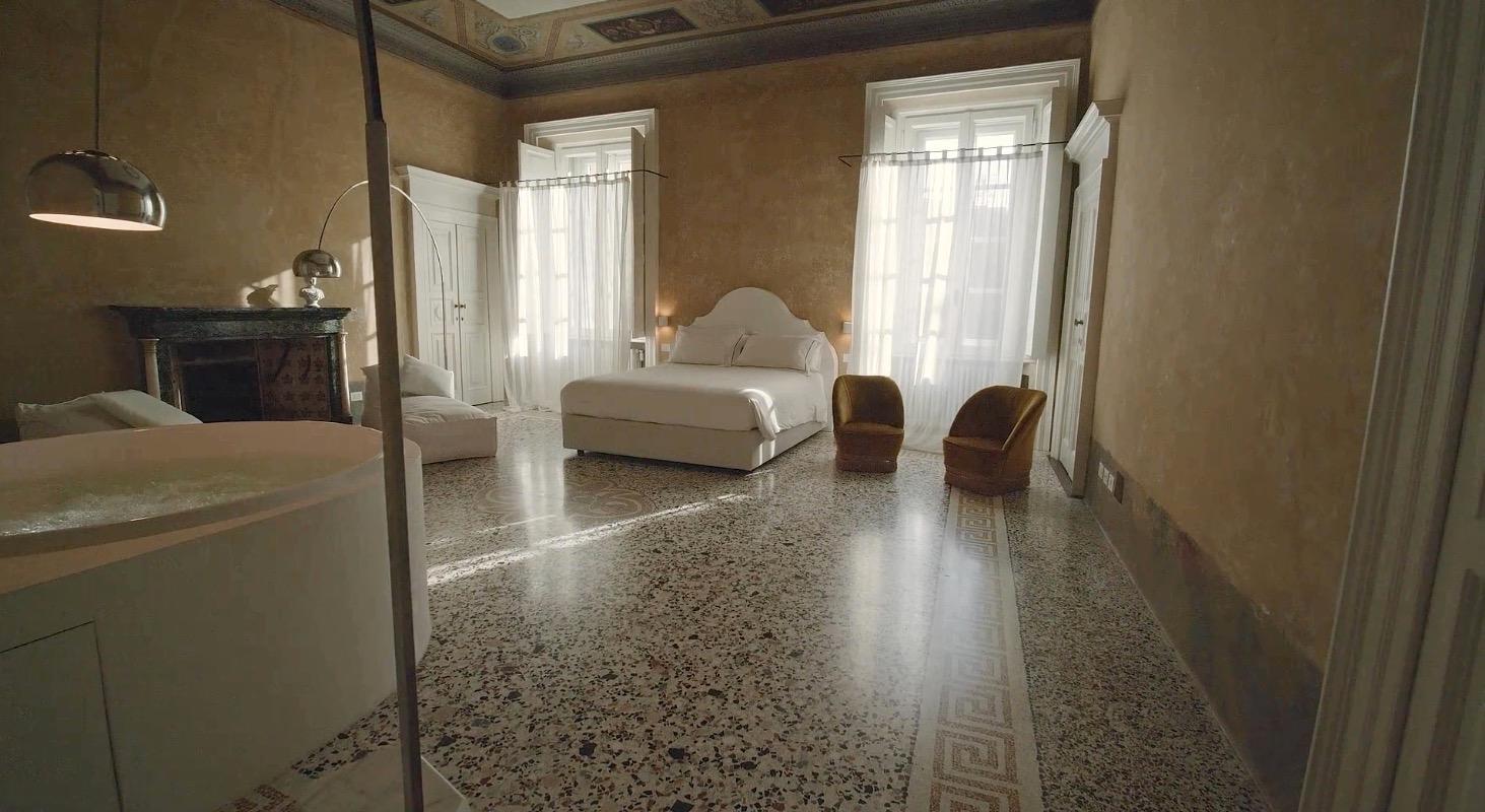 a frescoed bedroom with a freestanding bathtub, a canopy bed, a terrazzo floor and tall shuttered windows letting in daylight