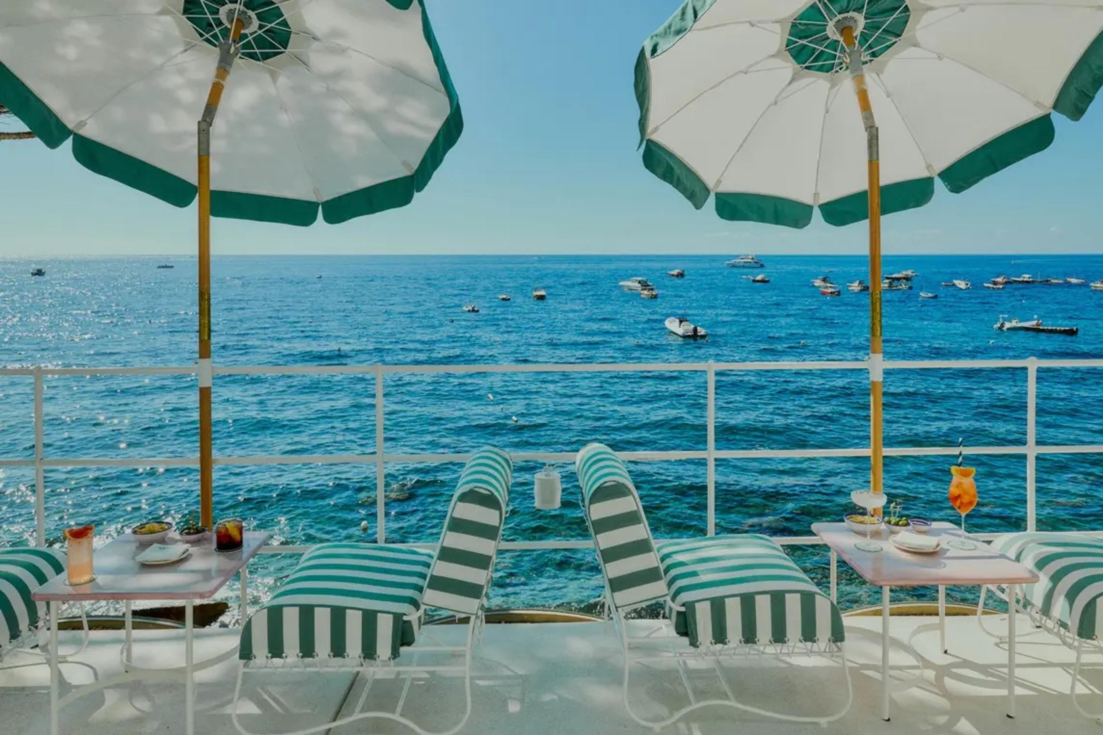Striped deckchairs and green umbrellas on a balcony over the sea.