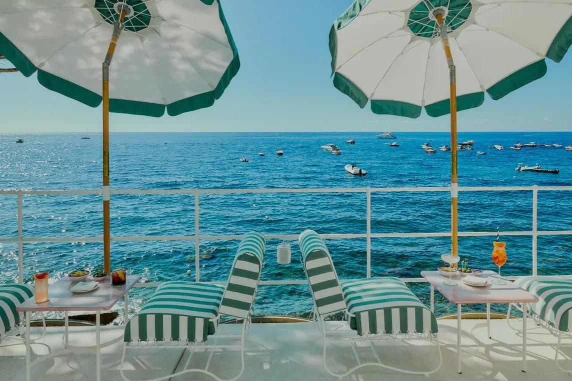 Striped deckchairs and green umbrellas on a balcony over the sea.