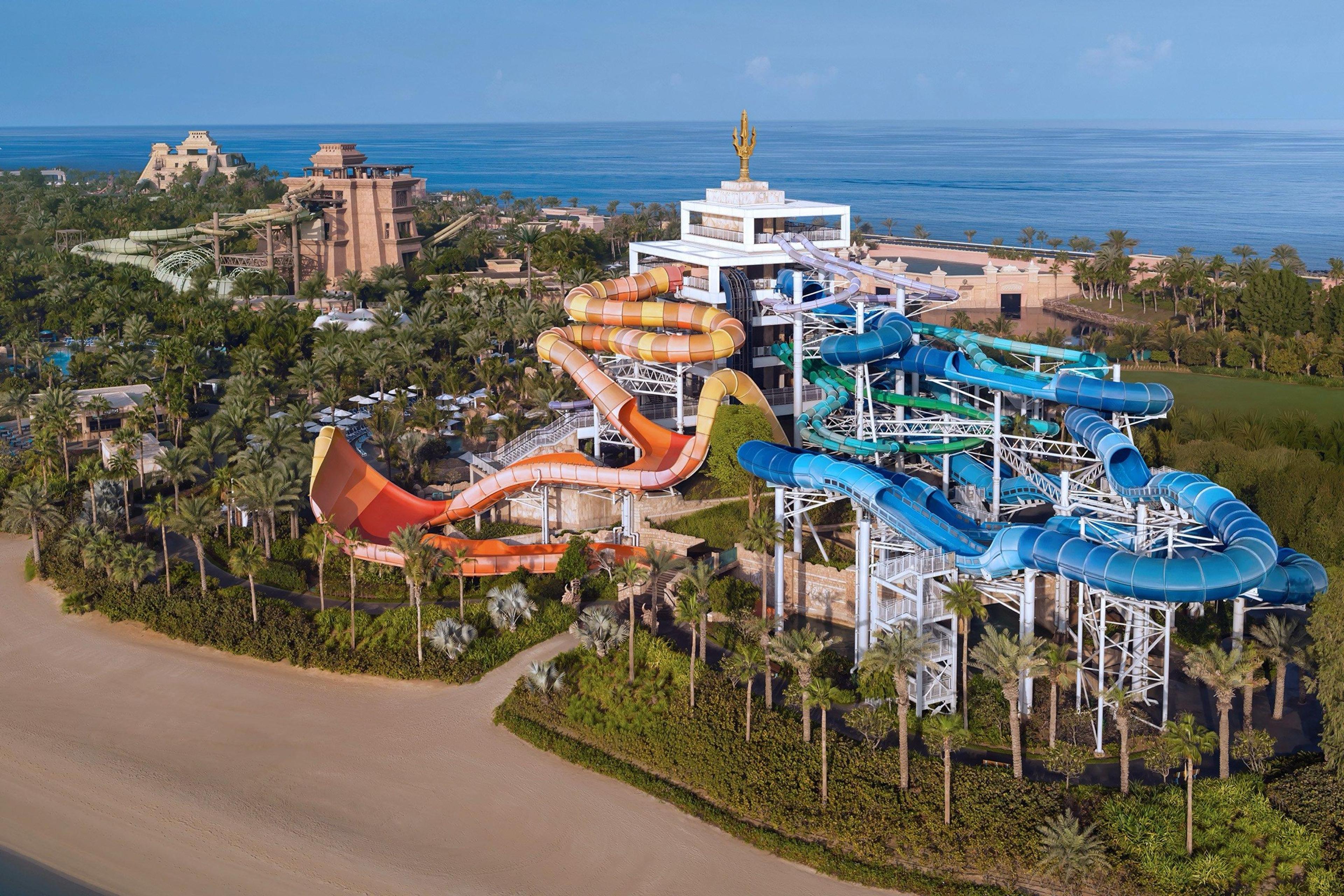An aerial view of the water park's tangle of orange, yellow and blue slide towers set among palm trees by the sea.