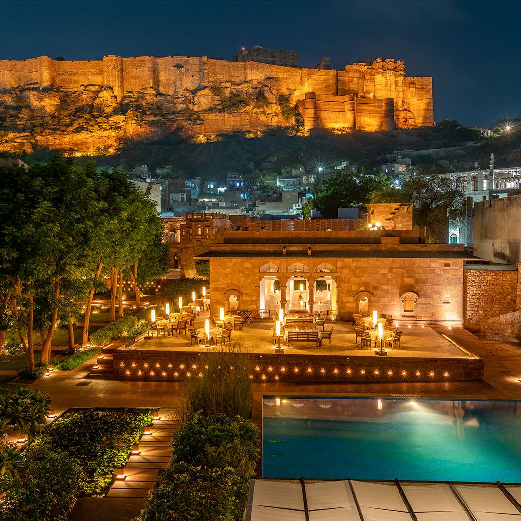A terrace lit at night, with the fort lit on the hill behind